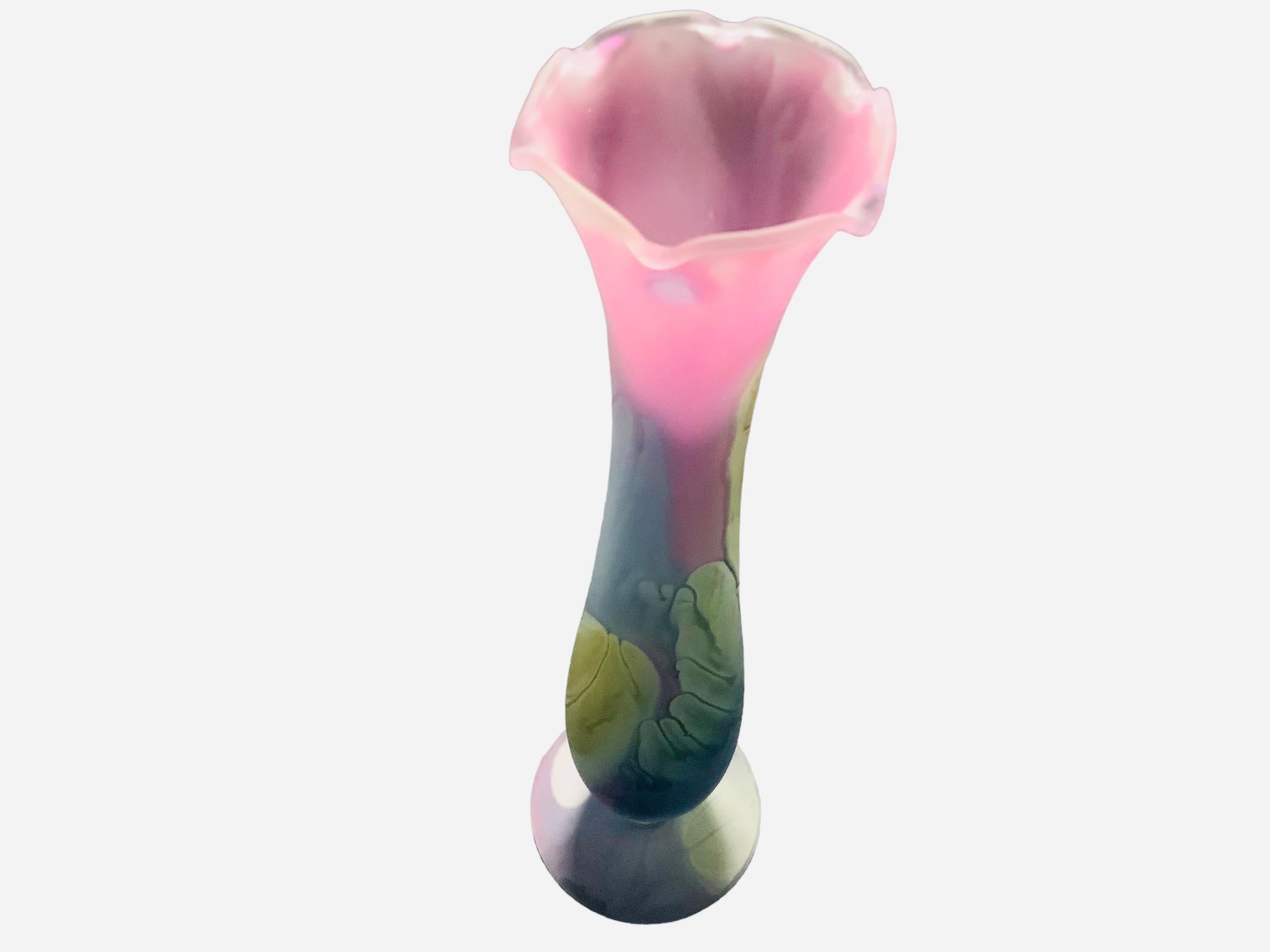 This is a Nouveau Art Rueven Glass Flower Bud Vase. It depicts an elongated pink, green-yellow, and grey blue amphora shaped bud vase with ruffles upper border. Below the base, it is the Nouveau Art Glass, Reuben Glass label.