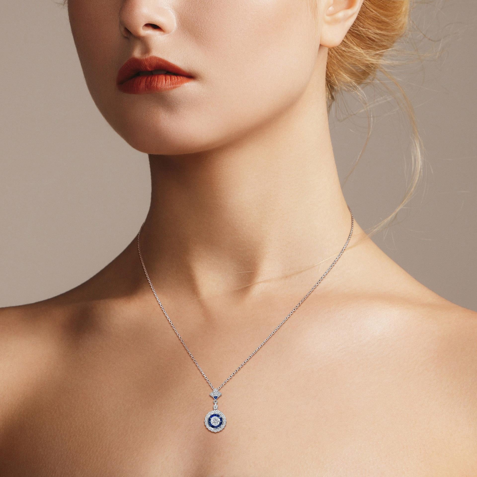 An Art Deco style diamond and sapphire pendant made with 18K white gold. The center diamond is a 0.25 Carat round cut of exceptional brightness. It is surrounded by sapphires that are cut by hand to fit seamlessly together. The sapphire is further