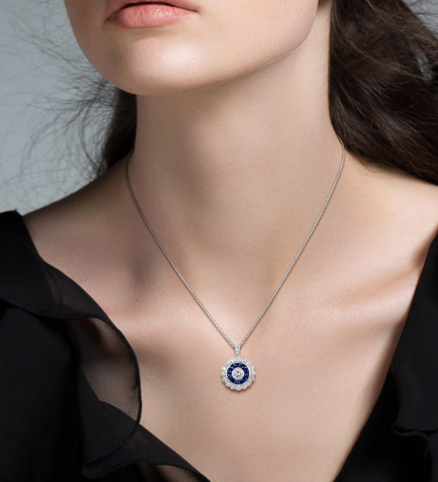 A glamorous pair of Art Deco-inspired target pendant bezel set with a round brilliant cut diamond in the center. The diamond weighs approx. 0.1 carat and its haloed by French cut sapphires and further diamonds set in 18k white gold with millgrain