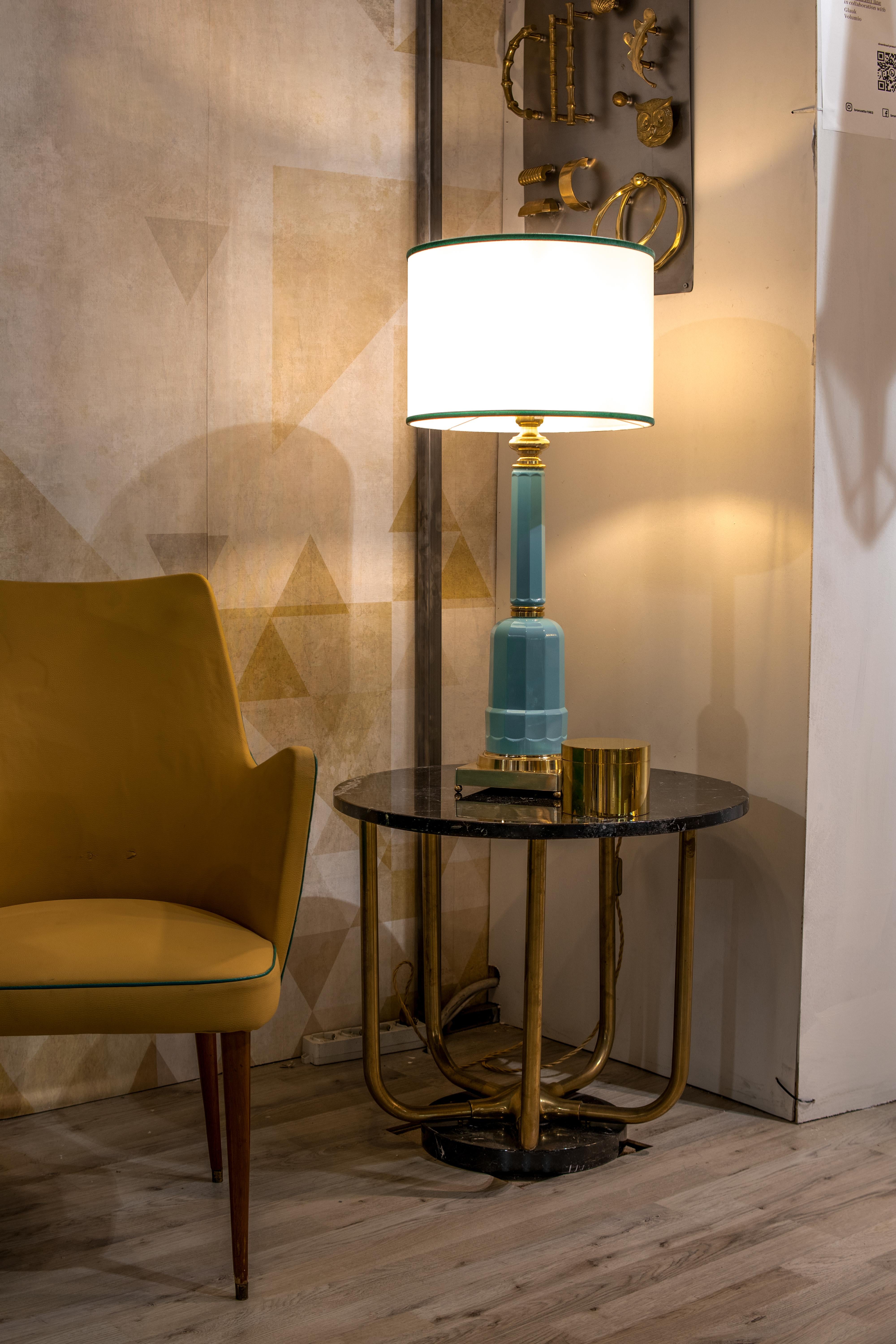The Jacaranda table lamp is made of blown glass with the base and details in brass, natural finish, and fabric lampshade. The glass structure is obtained with the artisan technique of glass blowing inside a mold, usually of wood or carved metal, in