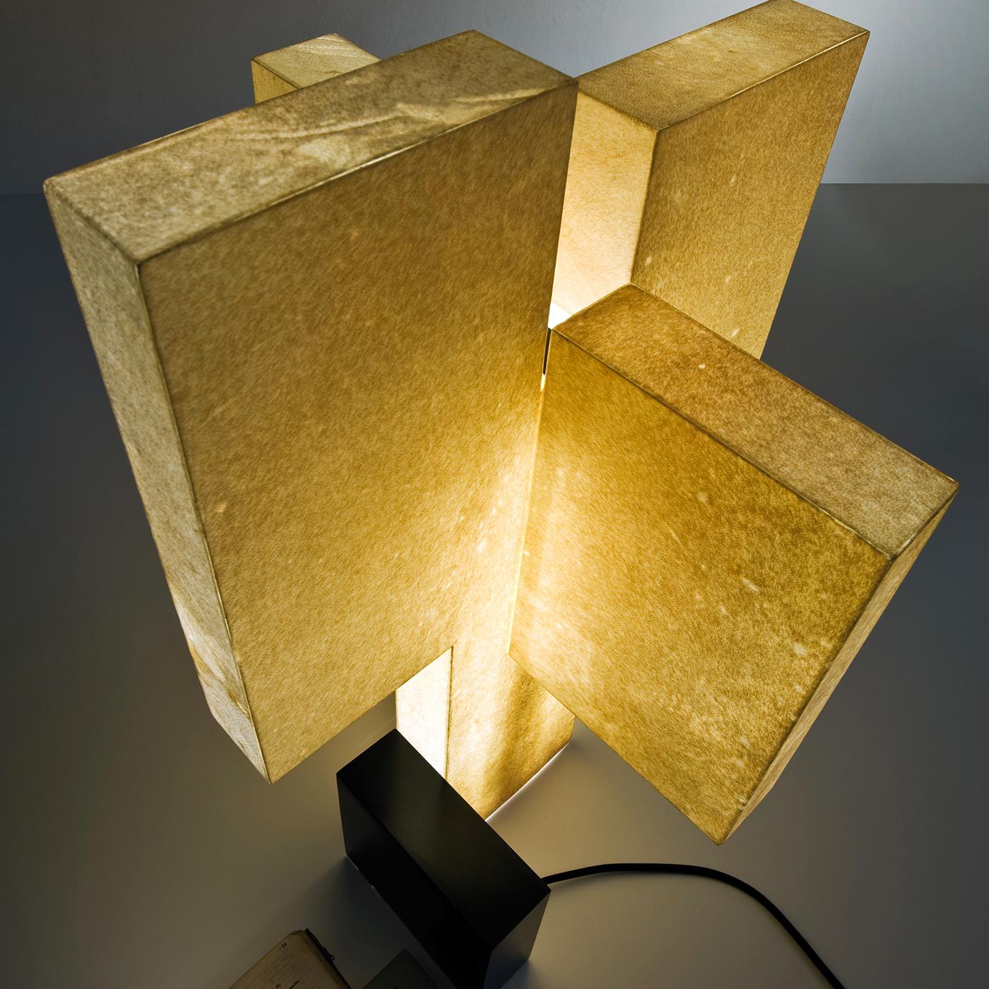 The sculptural design and imposing size of this exquisite table lamp make it a precious light source on a desk, side table, or entryway console. Its unique structure is made of brass with a burnished finish, methacrylate, and goatskin. Inside, the