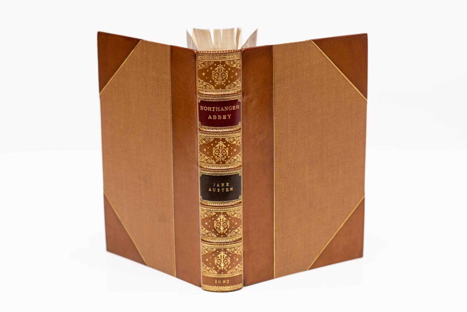 6 Volumes. Jane Austen. Novels, includes A Memoir and Lady Susan. Bound in 3/4 tan calf by Bickers & Son, linen boards, top edges gilt, raised bands, ornate gilt on spines, red and green labels, frontispiece in each volume. Published: