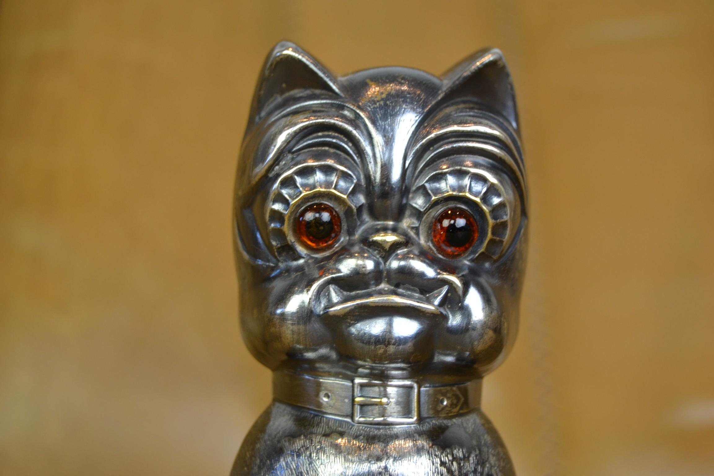Antique Silvered French Bulldog Money Box. 
This Money bank in the shape of a French Bulldog Dog was made in Germany circa 1920s. 
The Cubistic Bulldog has large orange brown glass eyes, wears a collar and is sitting on a treasury with lock. Under