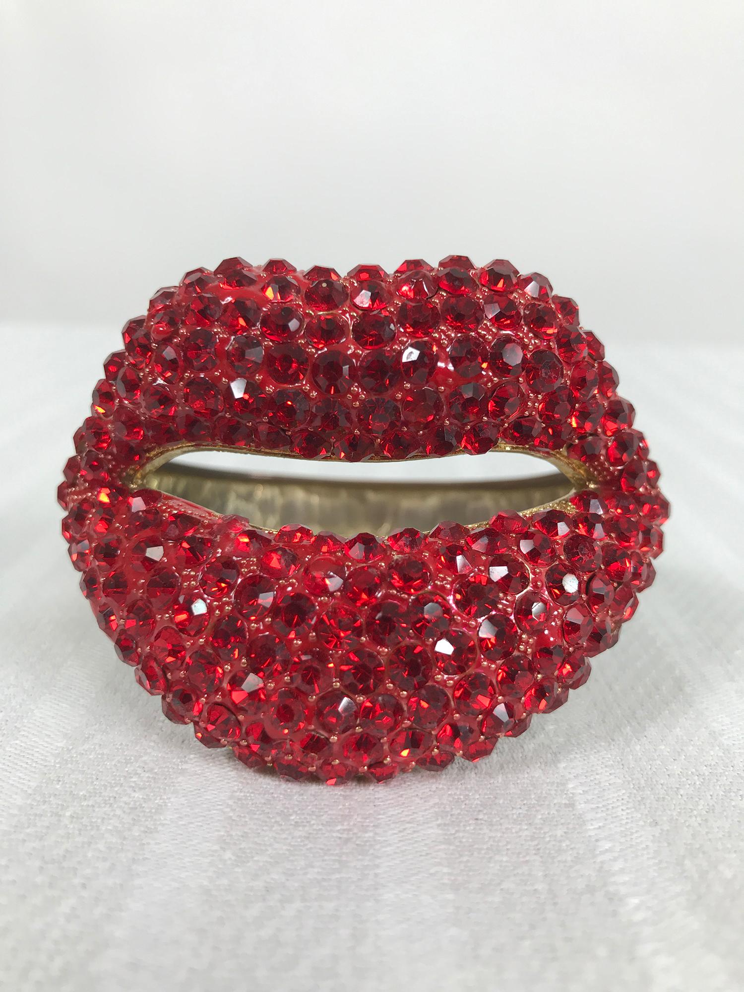 Novelty red rhinestone lips bracelet from the 1980s. Chunky gold metal camp bracelet, the front is a pair of open lips that are encrusted in large faceted red rhinestones, the back 1/2 of the bracelet is burnished gold metal. Spring hinge side, with