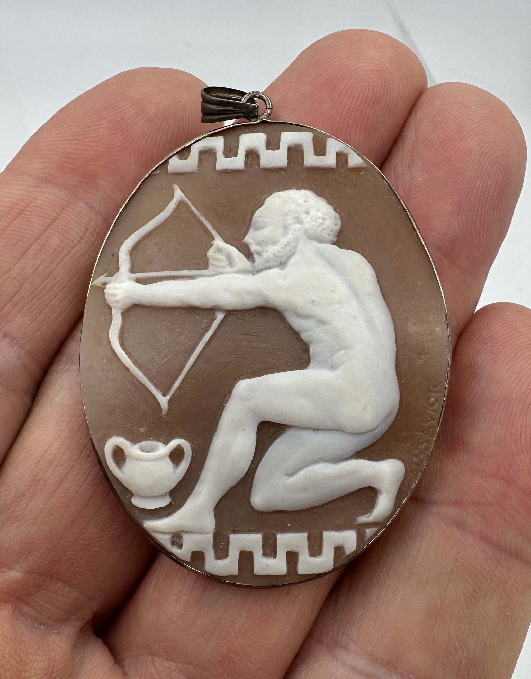 Indulge in a museum quality absolutely stunning and very rare large antique Shell Cameo Pendant Brooch with a hand carved image of a nude God Apollo with his Archery Bow and Arrow with a Greek Key motif at the top and bottom.   The large