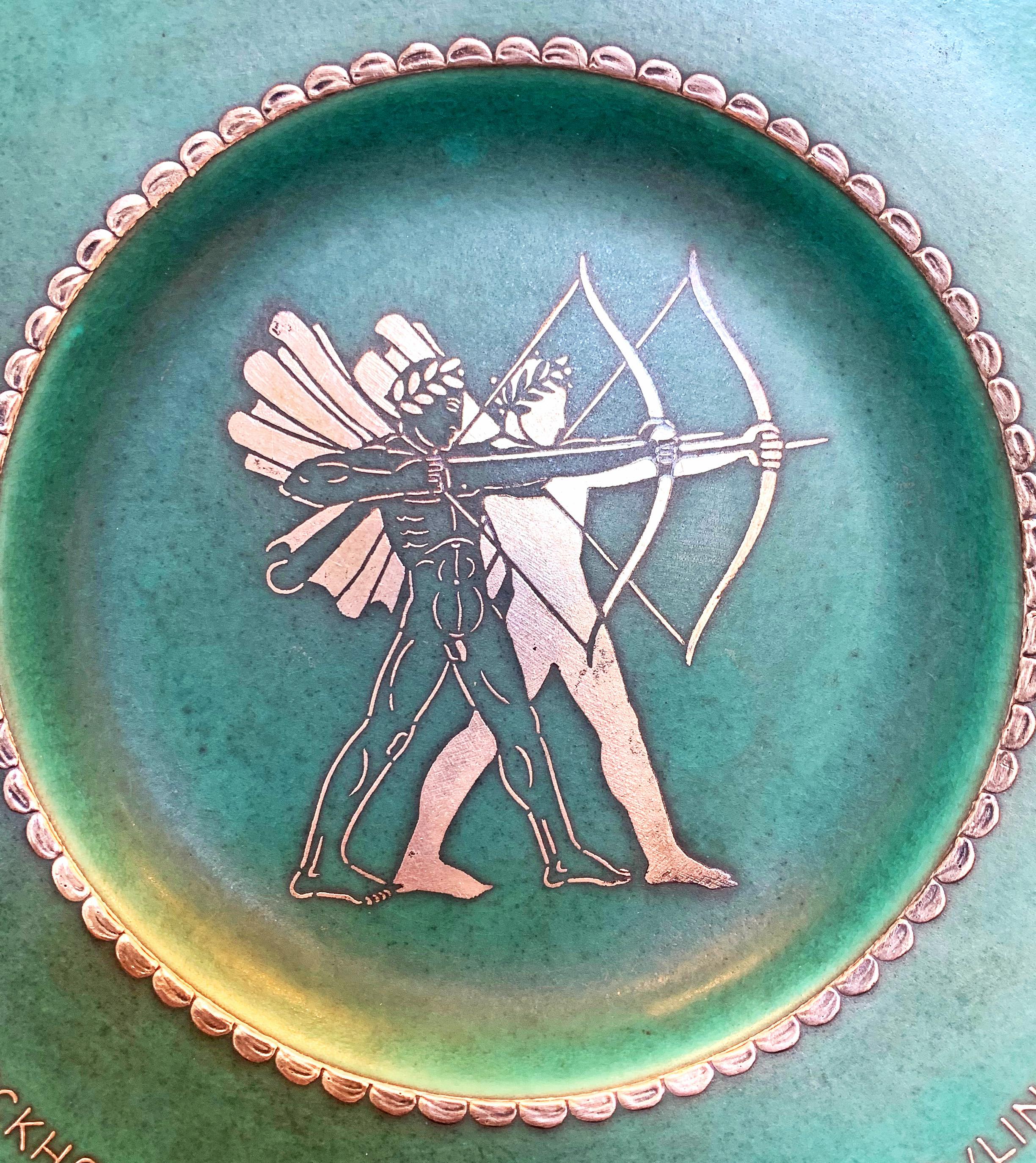 A rare and stunning example of the Argenta line of porcelain art wares produced by the Gustavsberg works in Sweden, characterized by a glowing, turquoise blue-green glaze decorated with silver overlay, this dish celebrates an archery event hosted by