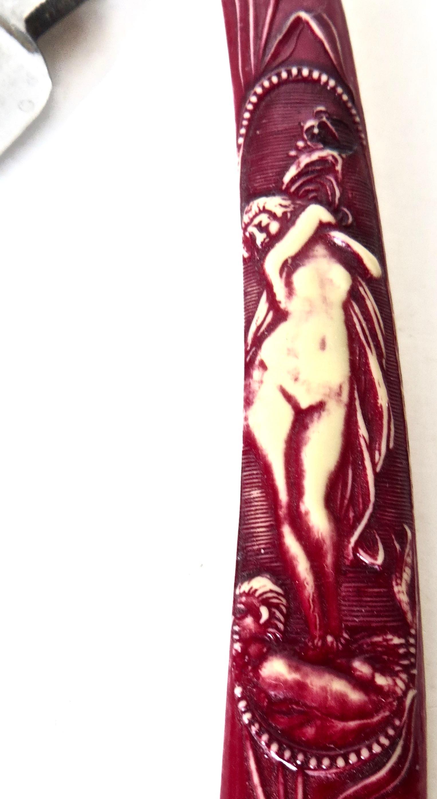 Great barber shop collectible item consisting of a German straight edge razor with a molded red celluloid handle; theme is a nude standing on a pillow holding flowers over her head. The back blade side reveals manufactured by 