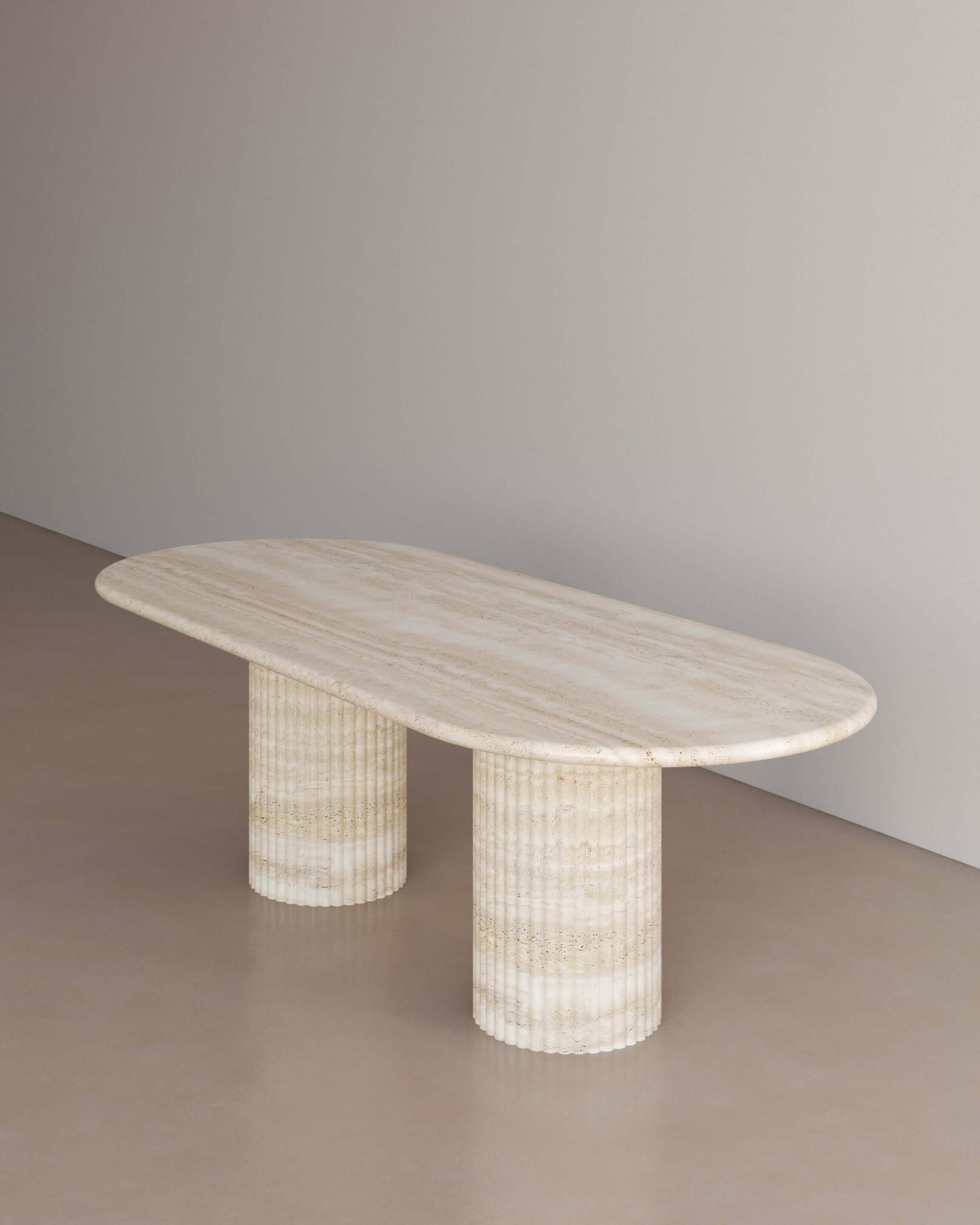 The Essentialist brings you The Antica Dining Table II in Nude Travertine. An oval table top resolved by smooth bullnose edges rests on two supporting pillars. Architectural form is refined by artistic expression echoing Roman culture. This table,