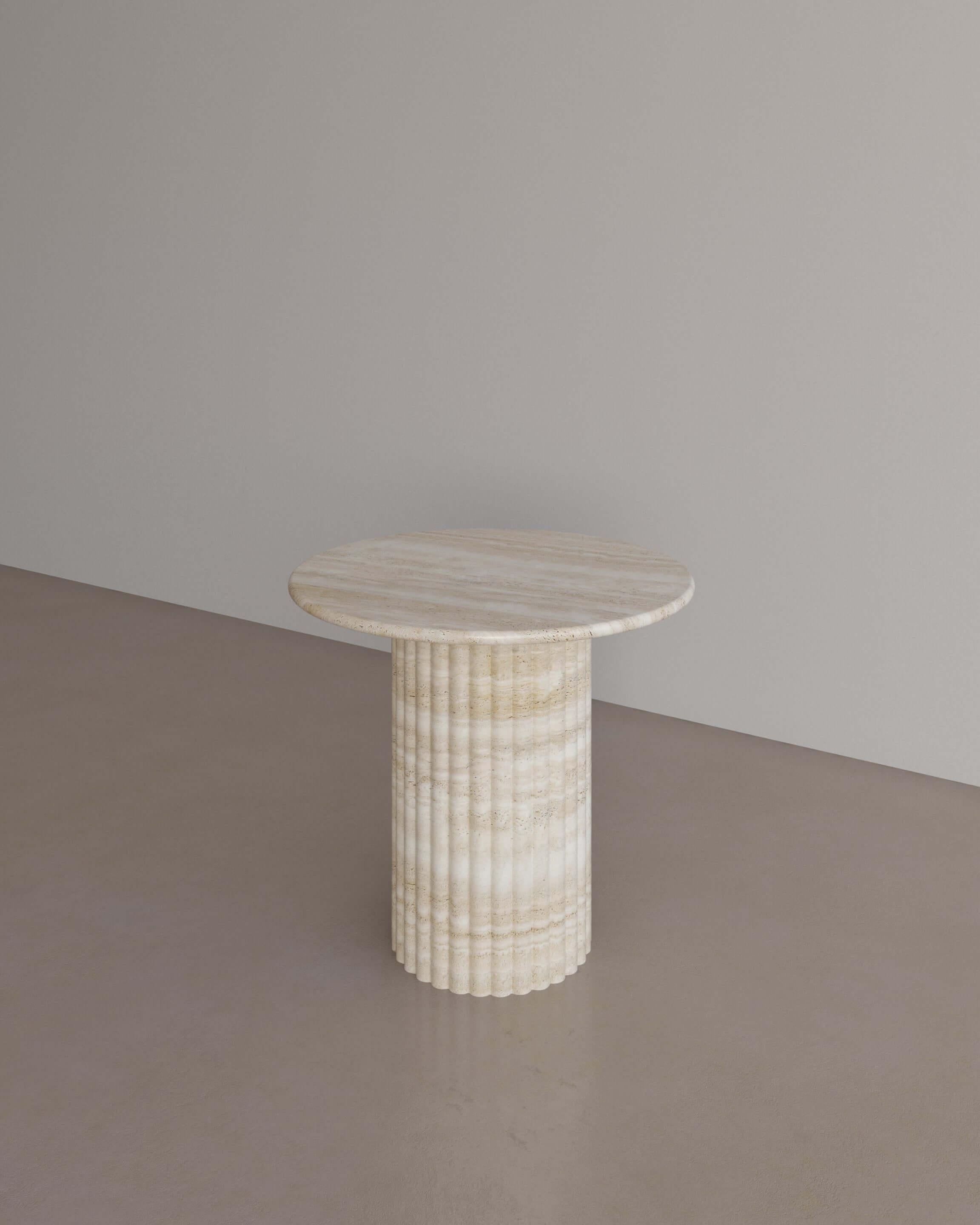 The Antica Occasional table in Nude Travertine by The Essentialist displays a perfect synergy by viewing classical idealism through a modern lens. A traditional pillar supports a circular top with bullnose edges, crafted from whole natural