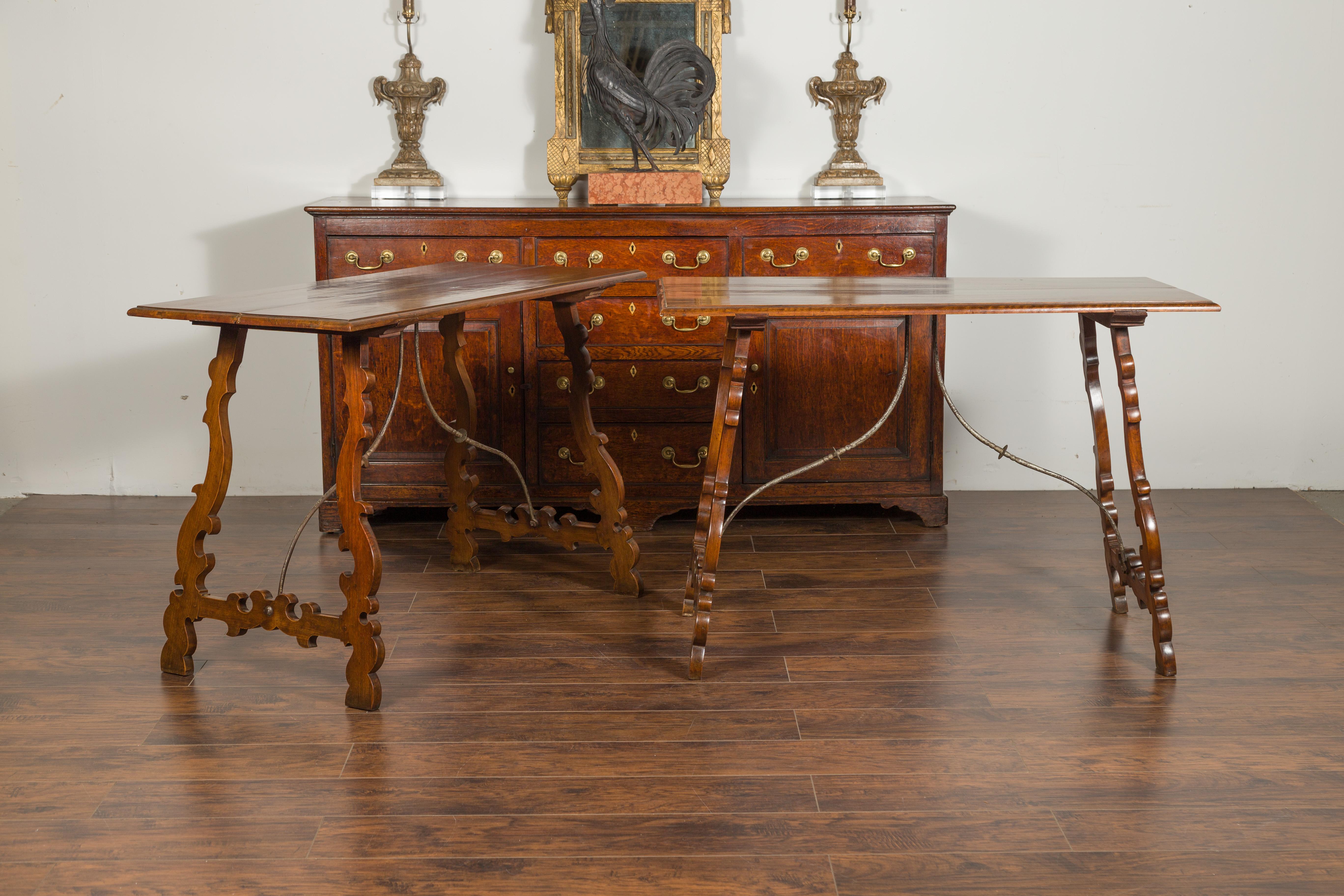 A pair of Spanish Baroque style walnut console tables from the late 19th century, with carved legs and iron stretchers. Created in Spain during the last quarter of the 19th century, each of this pair of console tables features a rectangular planked