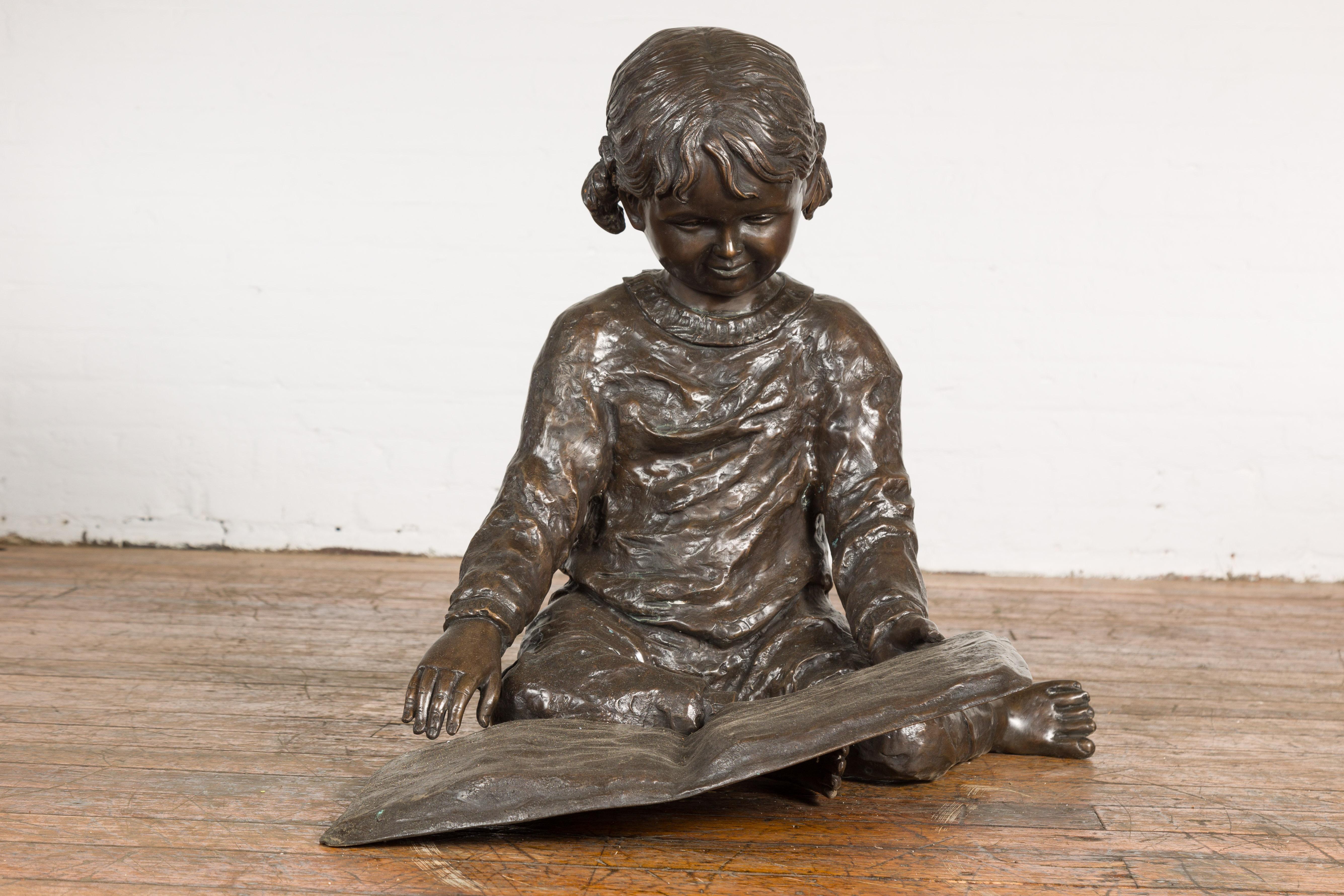 Eine im Wachsausschmelzverfahren gegossene Bronzestatue mit dem Titel Nursery Rhymes (Kinderreime), die ein kleines Mädchen darstellt, das auf dem Boden sitzt und ein Buch liest. Tauchen Sie ein in die bezaubernde Welt der Kindheit mit der 