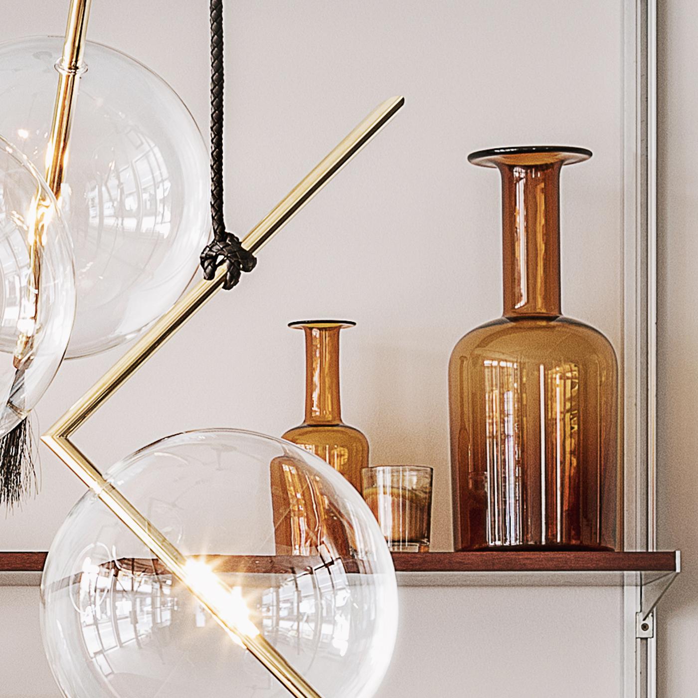 Marked by a streamlined silhouette and unconventional design, this exceptional light pendant will be a radiant touch in any interior. The set of five pendant lights boast a Minimalist shape, defined by a bent brass tube, accented with a hand blown