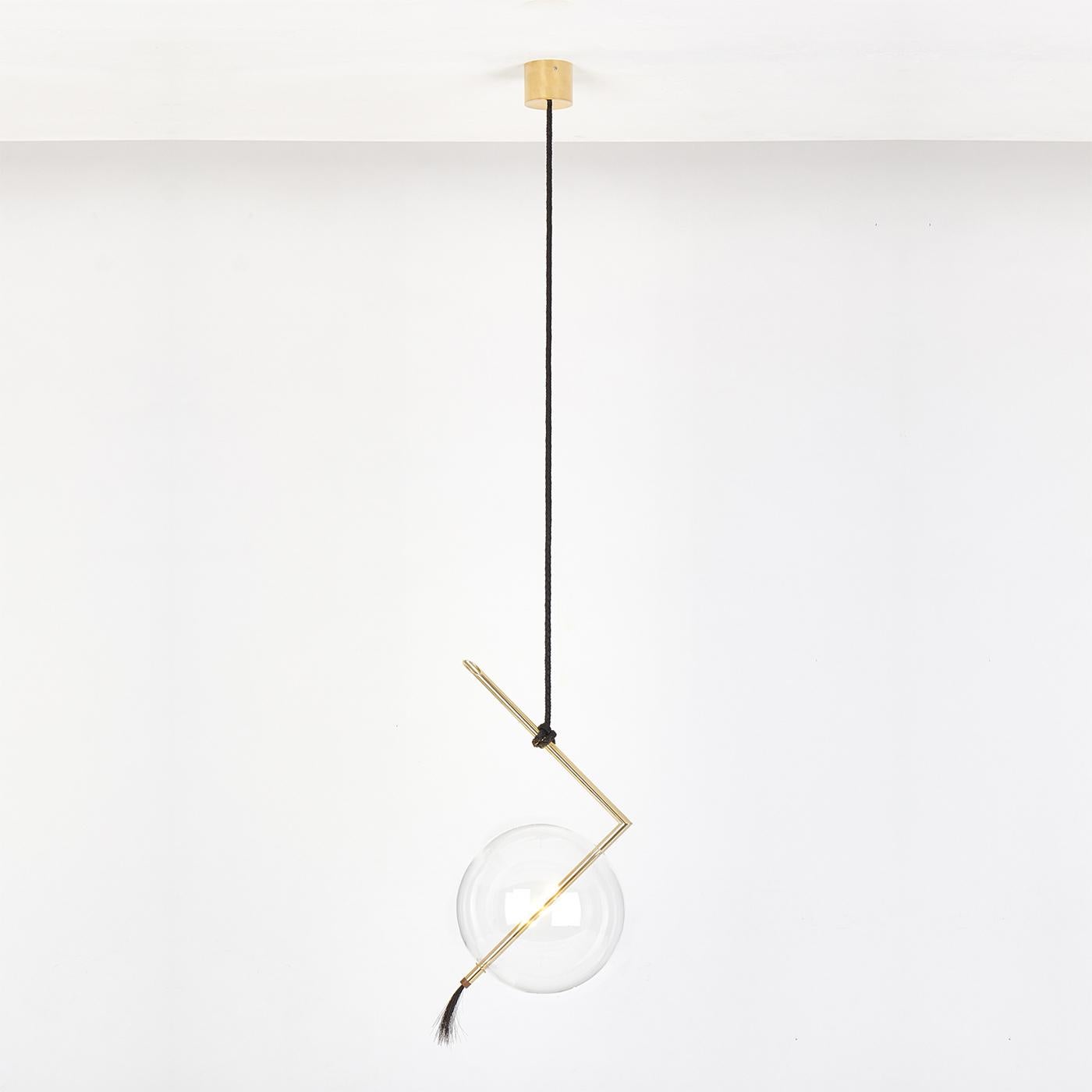 Arranged in multiples at different heights in a Minimalist living room or dining room, this refined light pendant is a radiant, sculptural statement piece. The unconventional Silhouette is made of a machined brass tube bent at a right angle, the top