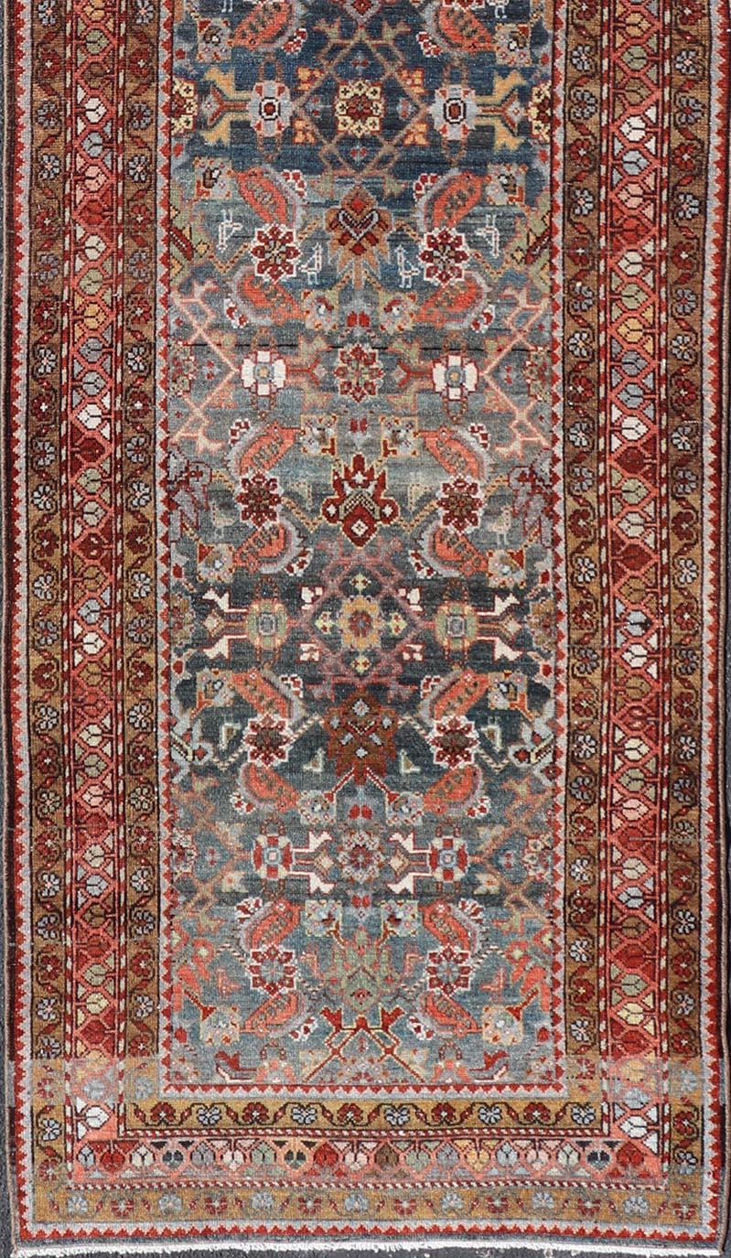 This Northwest Persian runner features a deep blue background flanked by multiple sand-colored and red borders. The elegant, all-over design in the field consists of a free-flowing pattern, reminiscent of geometric florals. The red, ivory, cream,