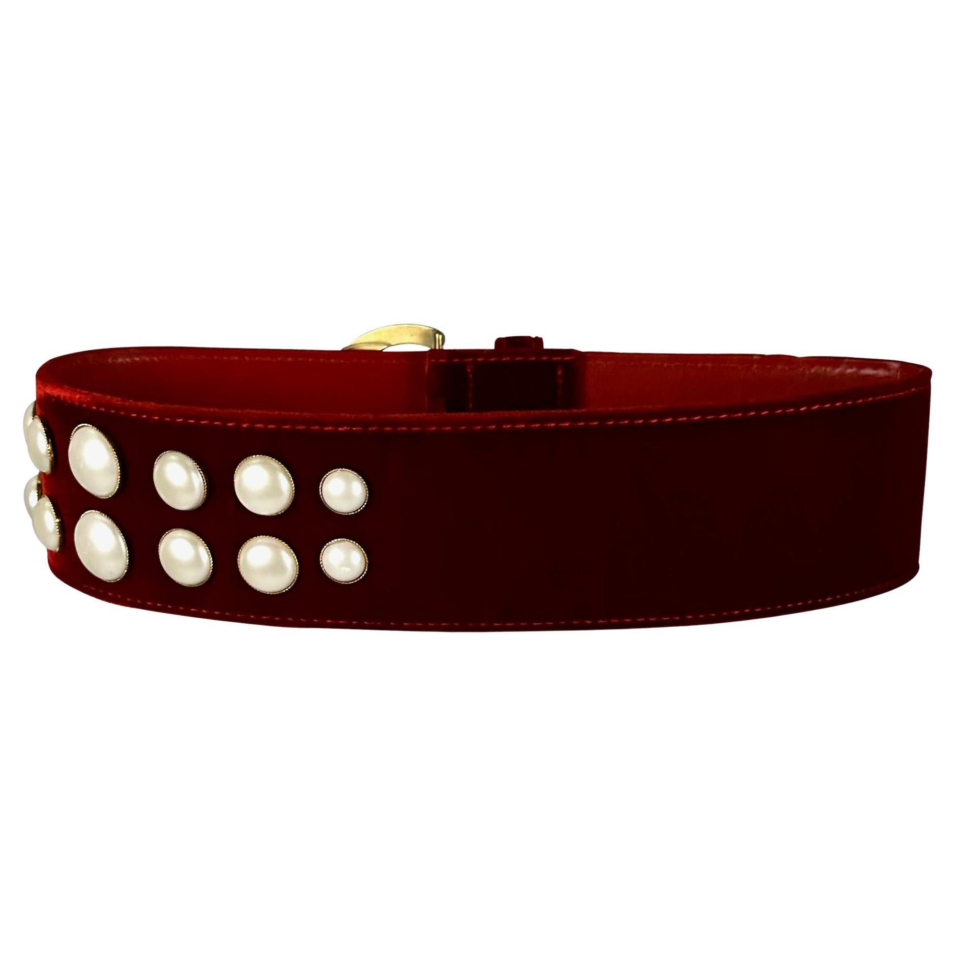 Presenting a fabulous red velvet Gianni Versace belt, designed by Gianni Versace. From the early 1990s, this incredible wide velvet belt features a gold-tone buckle and cluster of faux pearl accents. From over 30 years ago, this never worn belt is