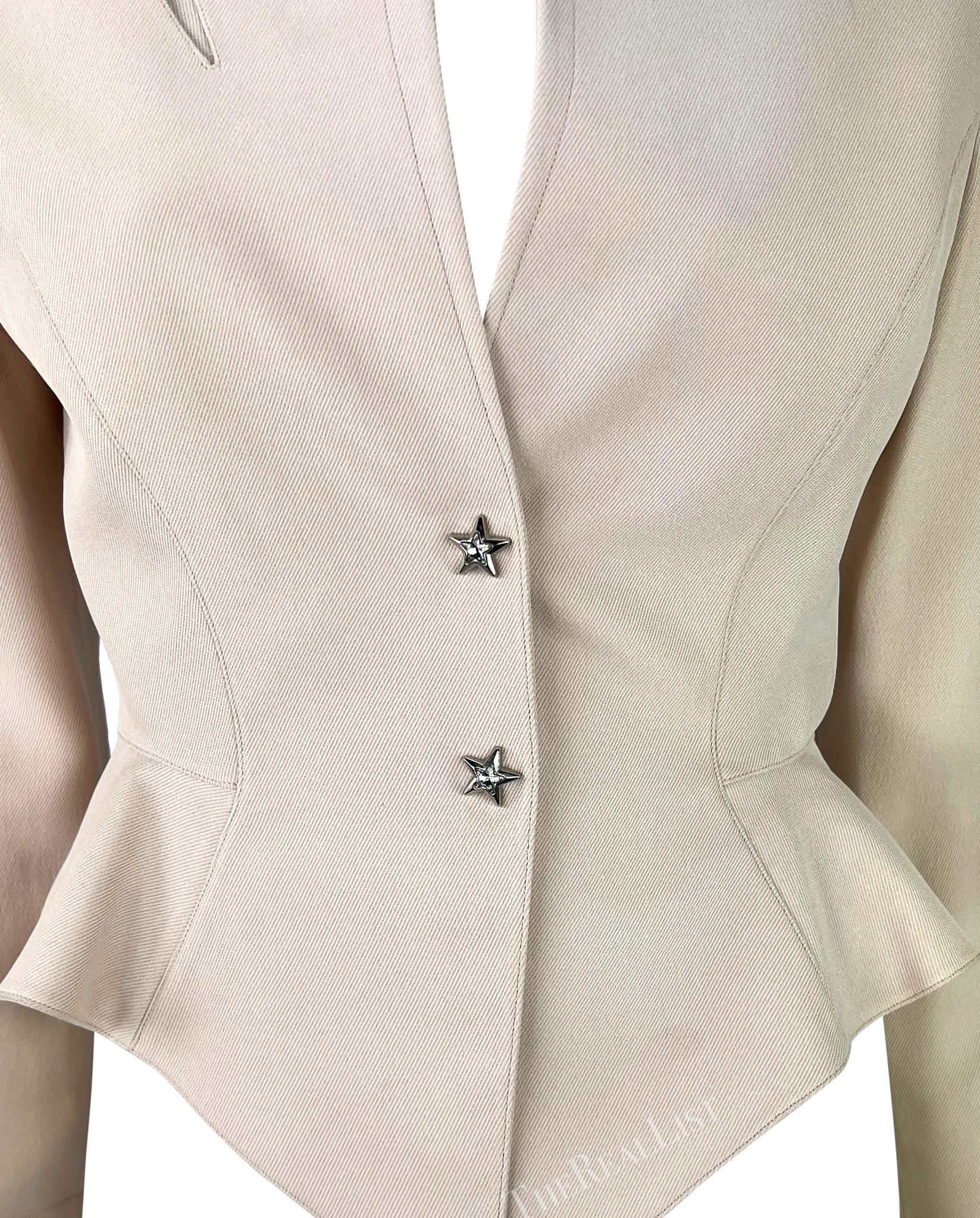 This light pink blazer by Thierry Mugler, designed by Manfred Mugler, is from the early 1990s. It has a sculpted look with a cinched waist, a light peplum, a small stand-up collar, and a plunging neckline. The shoulder features a lightning bolt