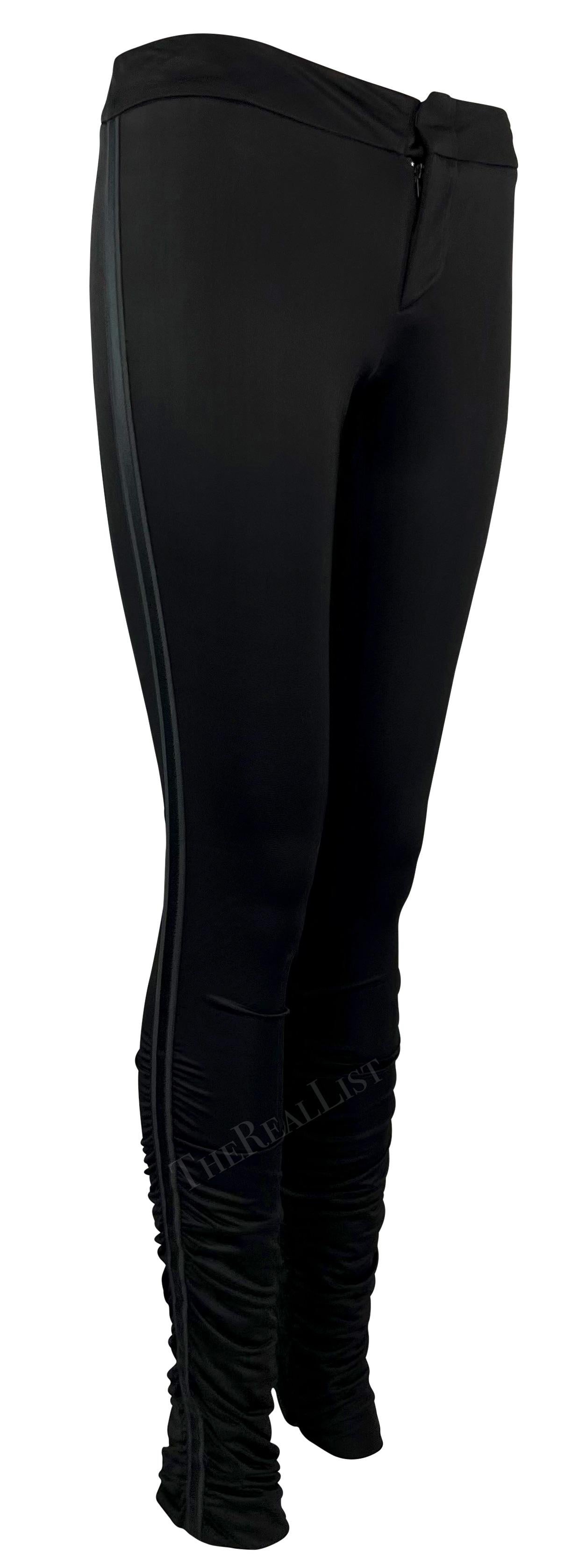 Ich präsentiere eine schwarze Gucci-Hose, entworfen von Tom Ford. Diese figurbetonte Satinhose aus der Herbst/Winter-Kollektion 2004 ist an den Waden gerafft und wird durch ein einfarbig gestreiftes Band an beiden Seiten vervollständigt. Diese