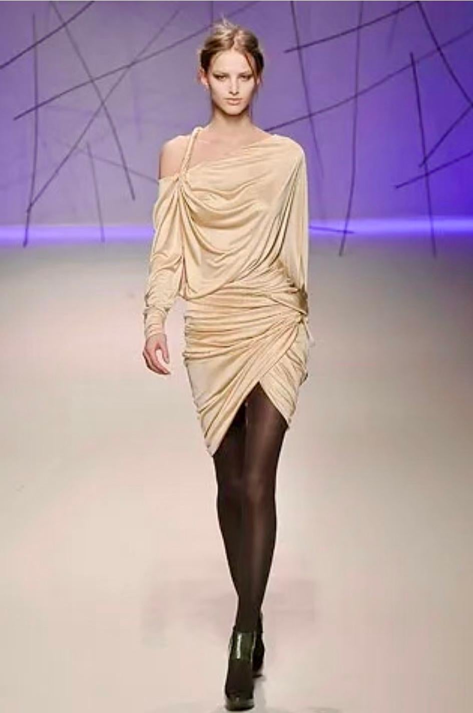 Dieses beigefarbene Viskose-Minikleid in Wickeloptik von Emanuel Ungaro, das im Herbst/Winter 2008 als Teil des Looks 20 auf dem Laufsteg debütierte, ist eine Meisterklasse in sanft drapierter Eleganz. Entworfen von dem kolumbianischen Designer