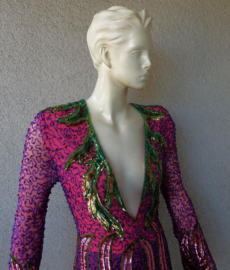 Gucci hand beaded silk evening dress adorned in contrasting shades of purple and rasberry pink accented in green beads brilliantly highlighting the magnificent artwork of the dress.  Fashioned with deep plunging neckline long slender scallop sleeves