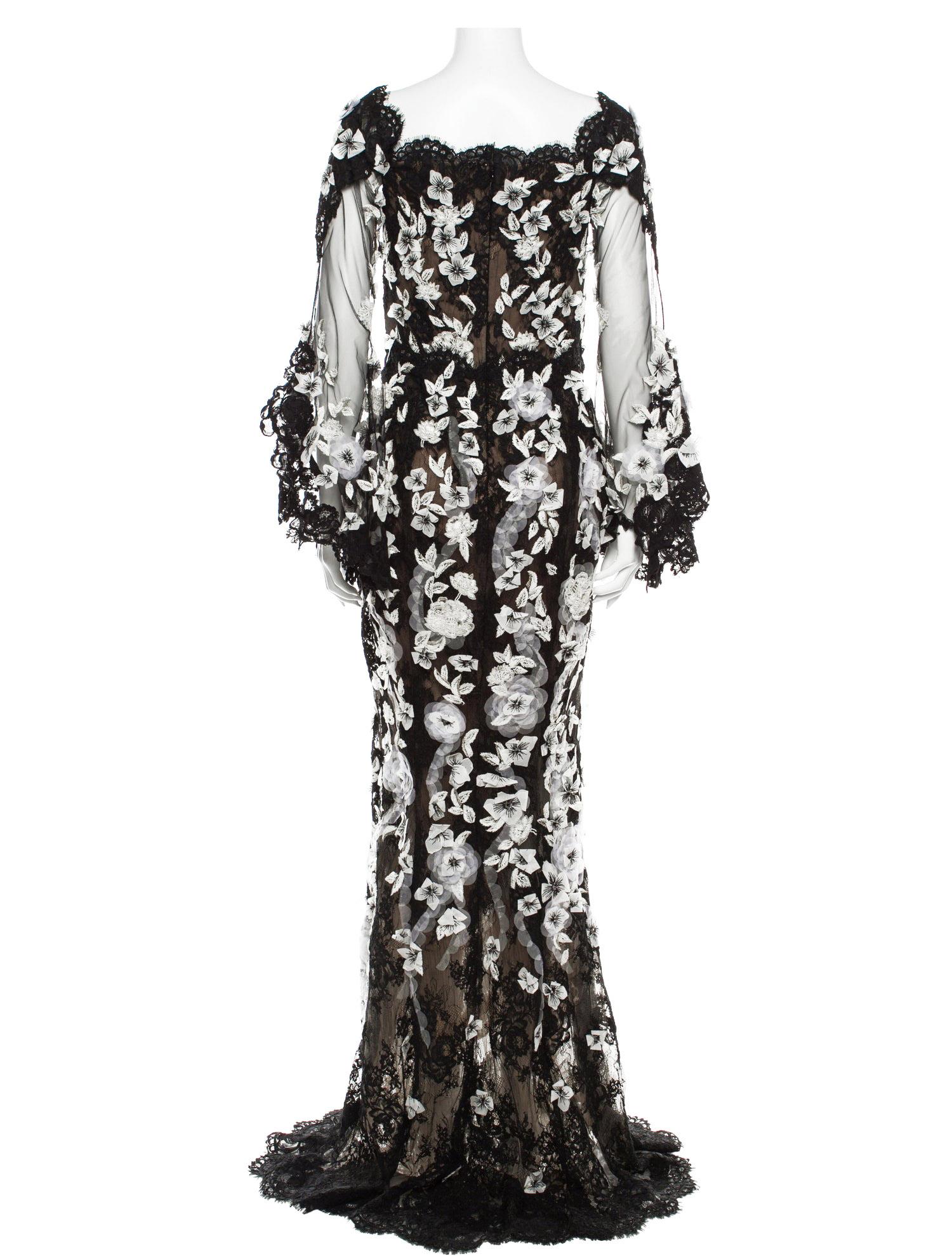 Une robe exquise Marchesa Pre-Fall 2019, mettant en valeur les détails romantiques signature de la maison. Cette création longue comme le sol est réalisée en dentelle noire transparente, entièrement brodée à la main de motifs floraux blancs