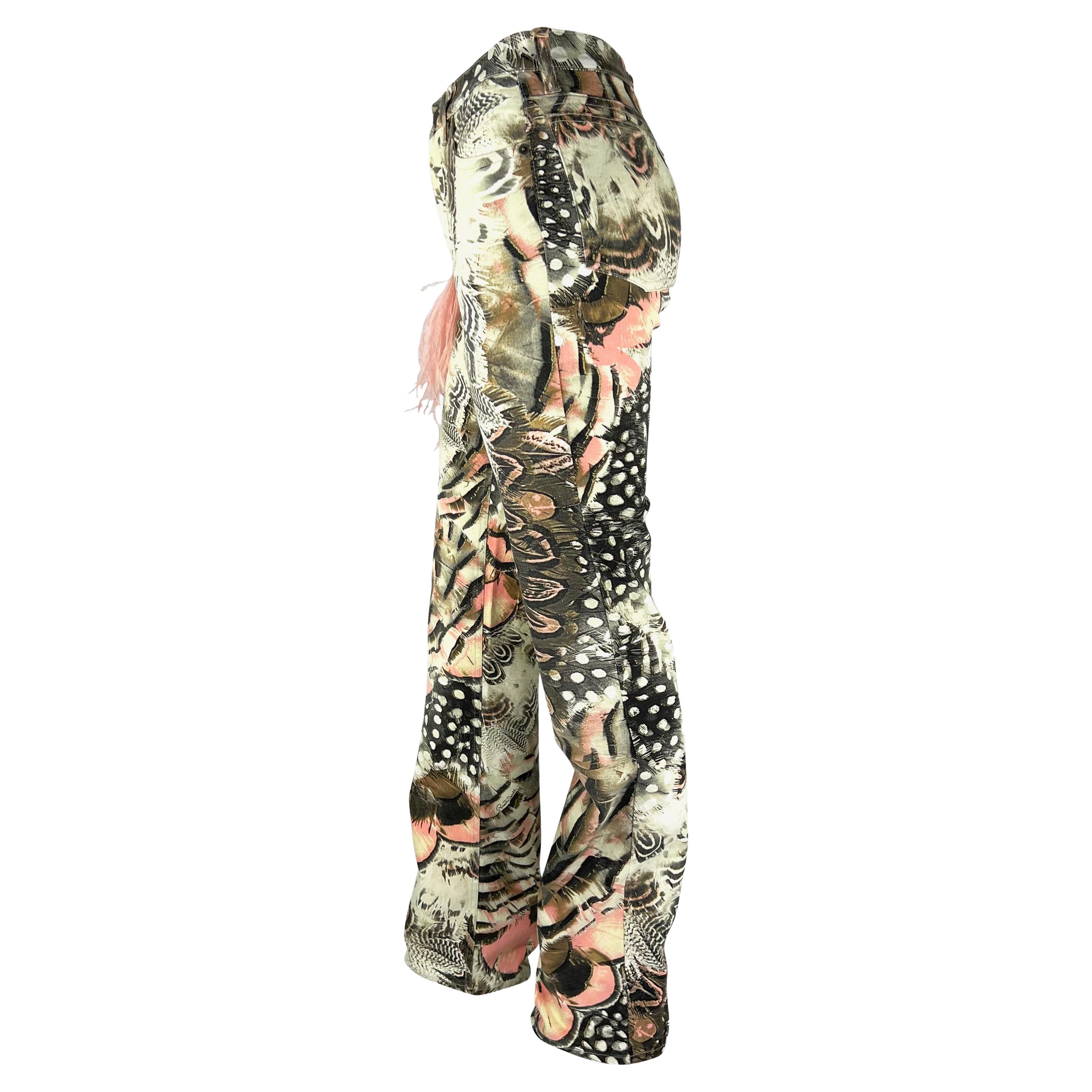 Presenting a pair of bright feather print denim Roberto Cavalli pants. From the Spring/Sumer 2004 collection, these pants feature several overlapping feather prints throughout and are amped up with a pink feather charm at the front belt loop. Never