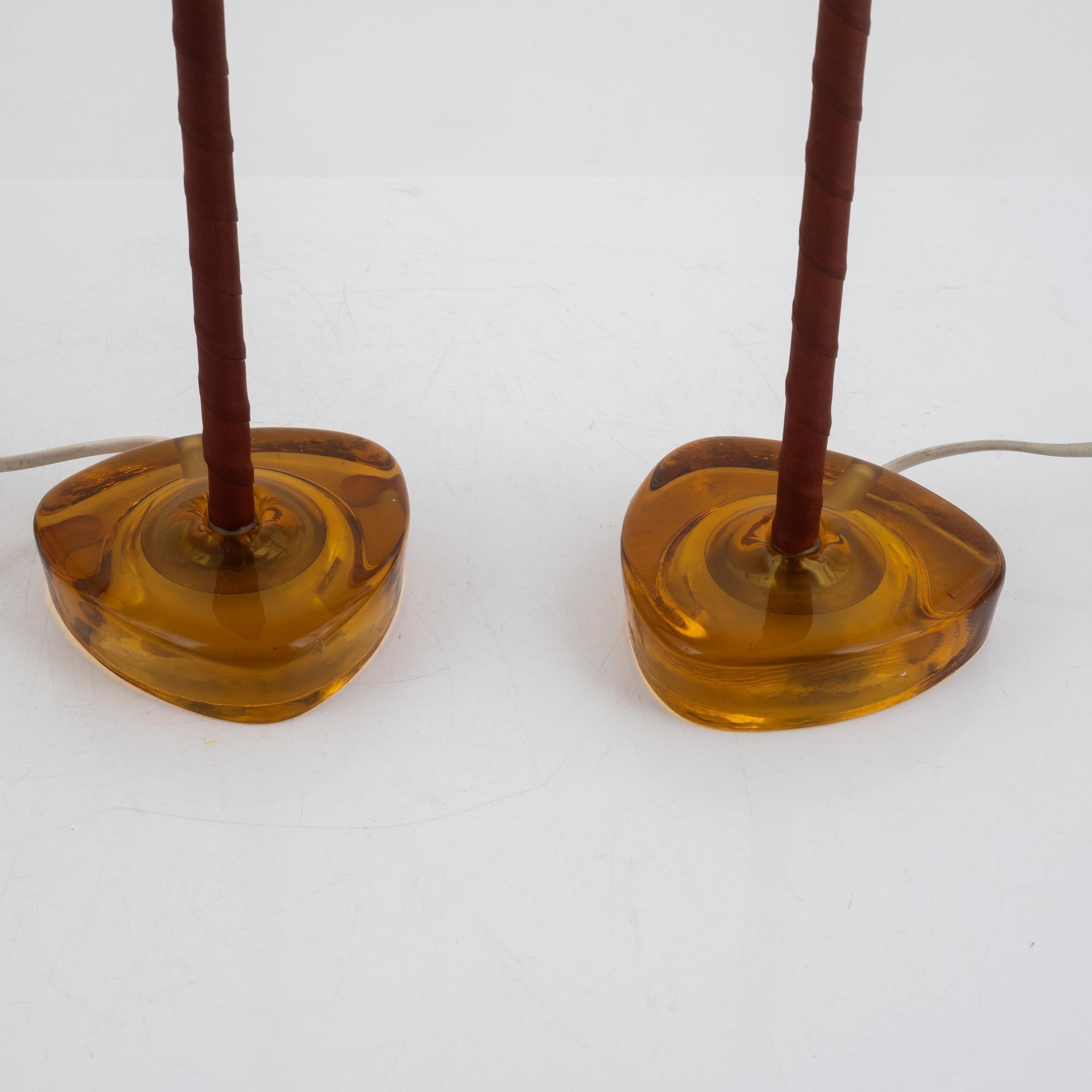 A pair of brass and amber color cast glass table lamps designed and produced by ANF Nybro Armaturfabrik, Sweden, c. 1960s.  Dimensions of Lamp (inches): 13.5” H x 4.25”  Diameter.
The brass lamp is covered by brown leather in good condition.