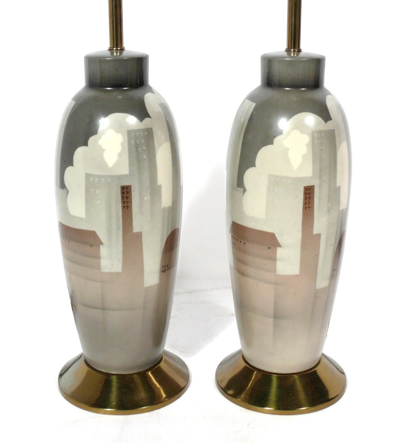 NYC cityscape pottery lamps, American, circa 1940s. They feature ceramic bodies, with brass hardware, and retain their original fabric shades and finials. They have been rewired and are ready to use.