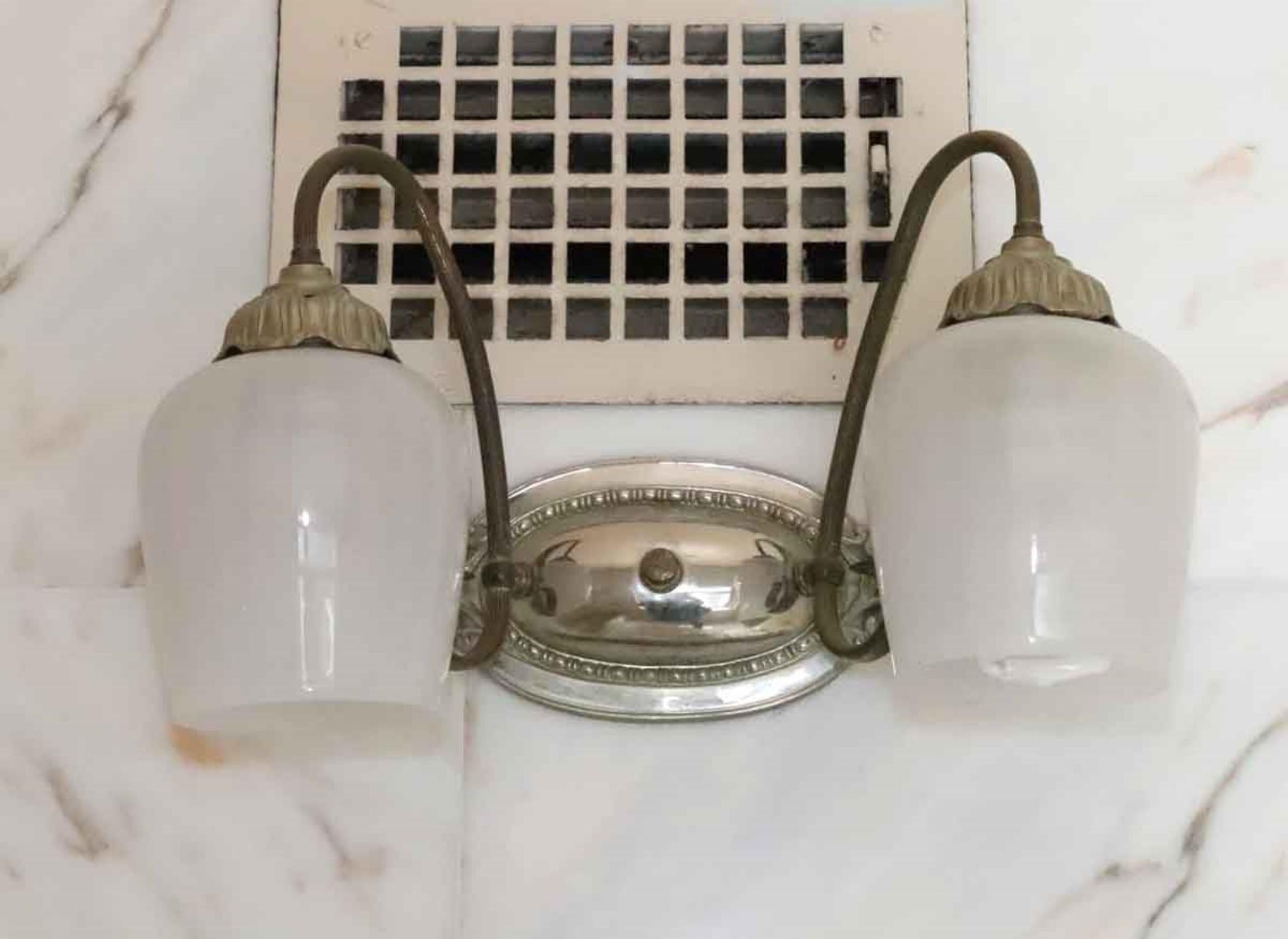 These Art Nouveau style wall sconces once adorned the famous Waldorf Astoria Hotel in New York City. They feature a nickel over brass oval wall mount with two brass arms each with a white milk glass tulip down shade. Waldorf Astoria authenticity