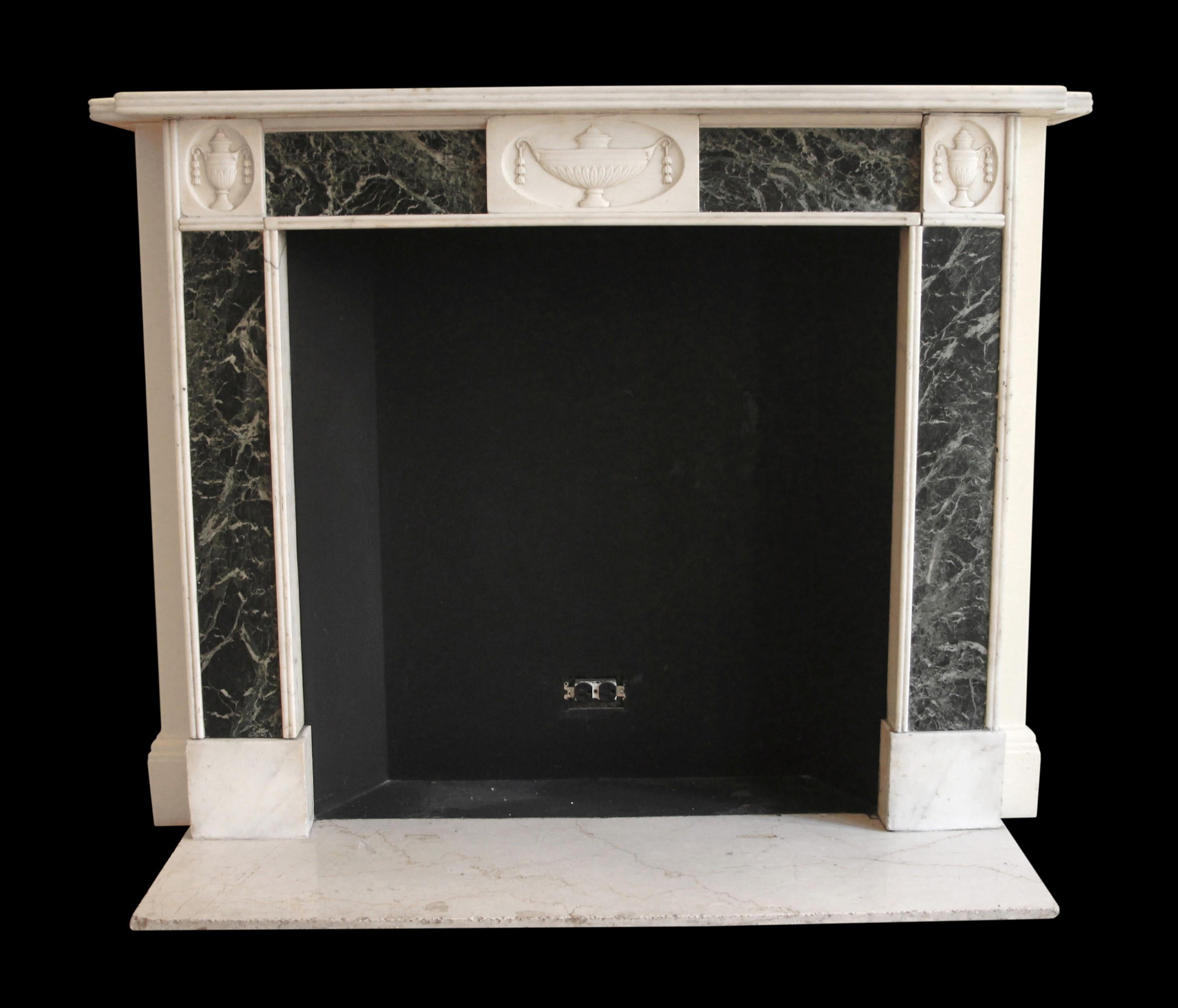 Early 20th century Neoclassical style Verde Antico green and white marble mantel featuring three hand carved urn motifs in the top two corners and center. This antique mantel was brought over from Europe to furnish the newly built Waldorf Astoria