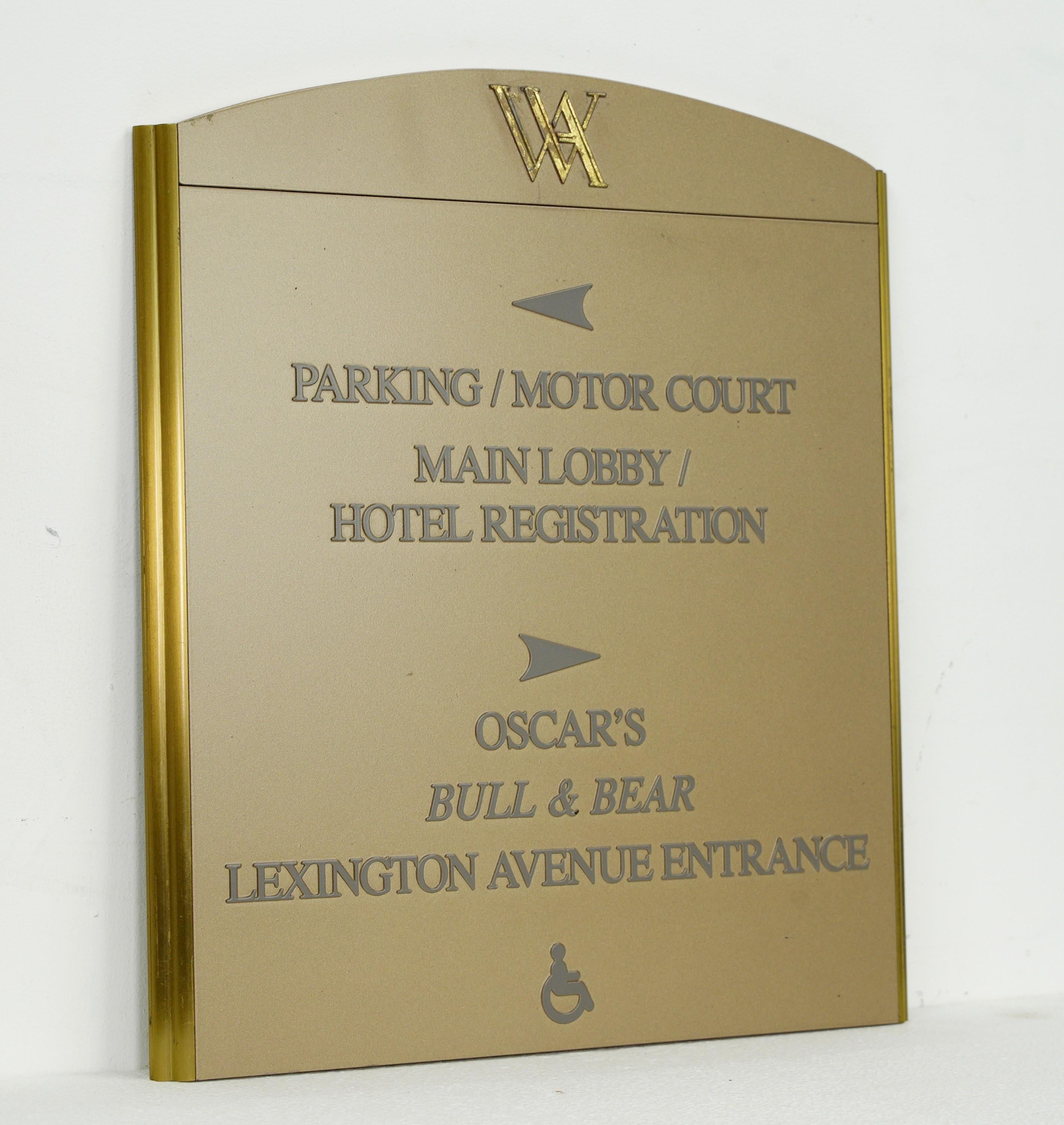 This Late 20th Century sign was sourced from the iconic Waldorf Astoria in New York City. The directional cues are painted on durable plexiglass, and framed by a brass border. Perfect for adding a touch of nostalgia to any space, this sign is a