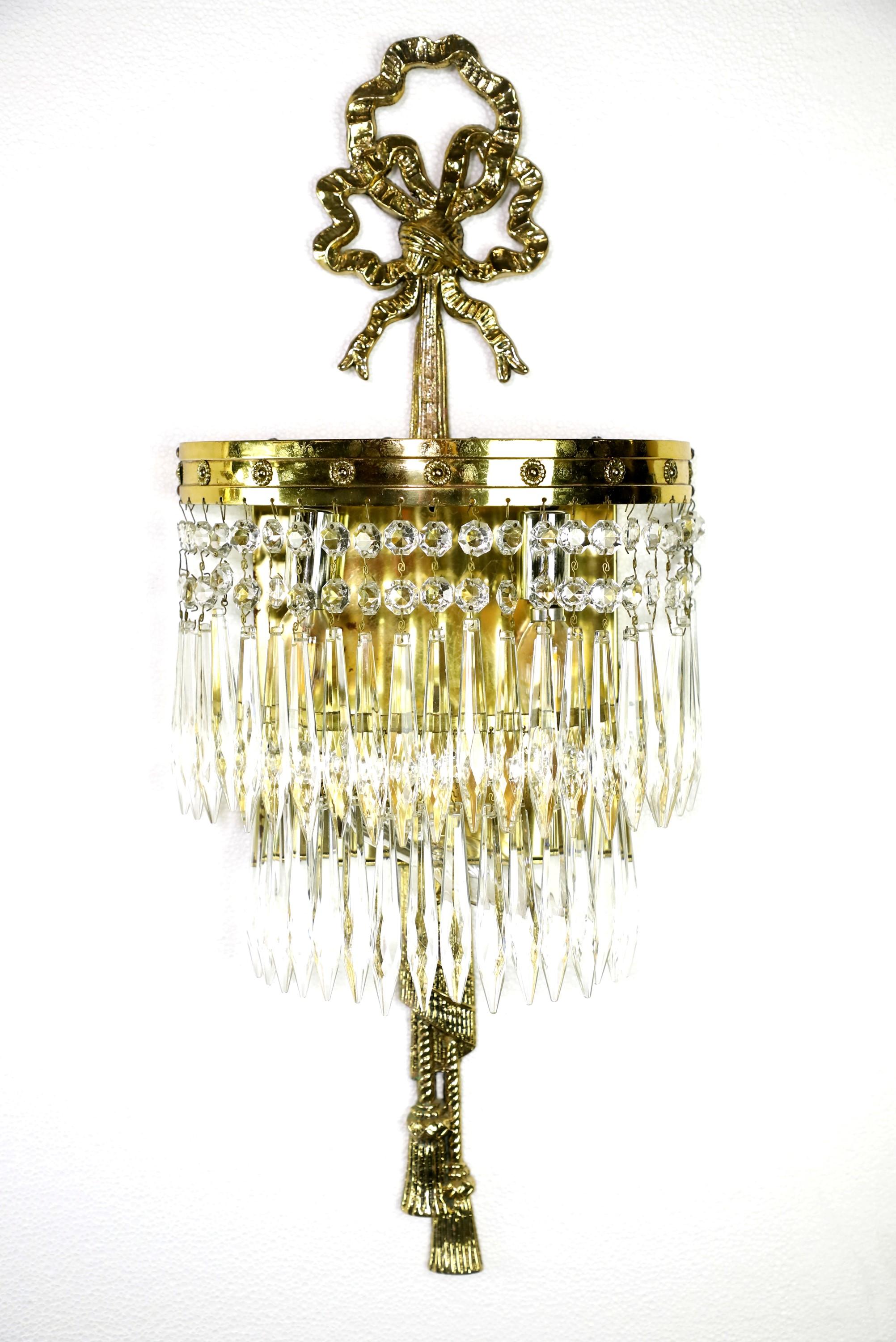 20th century pair of wall sconces sourced from the NYC Waldorf Astoria Hotel Park Ave South conference room. Regency style clear crystal wall sconces featuring a polished brass ribbon and tassel frame design. Cleaned and restored. Each sconce take