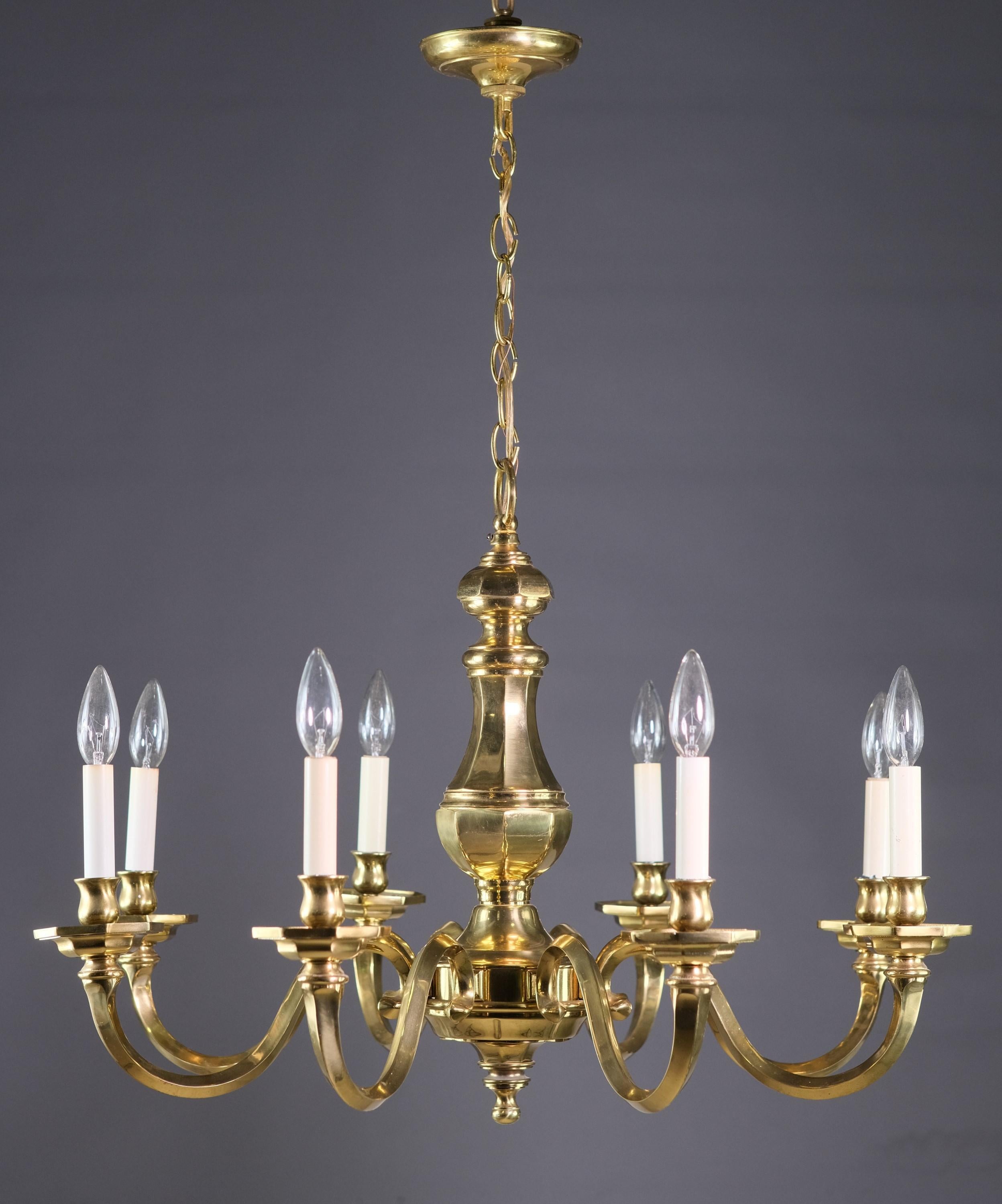 1980s Williamsburg style brass chandelier featuring an octagon shaped body and matching bobeches.   There are eight arms which are of a heavy cast brass with candlestick lights.  It originated from the 41st floor suite A of the NYC Waldorf Astoria