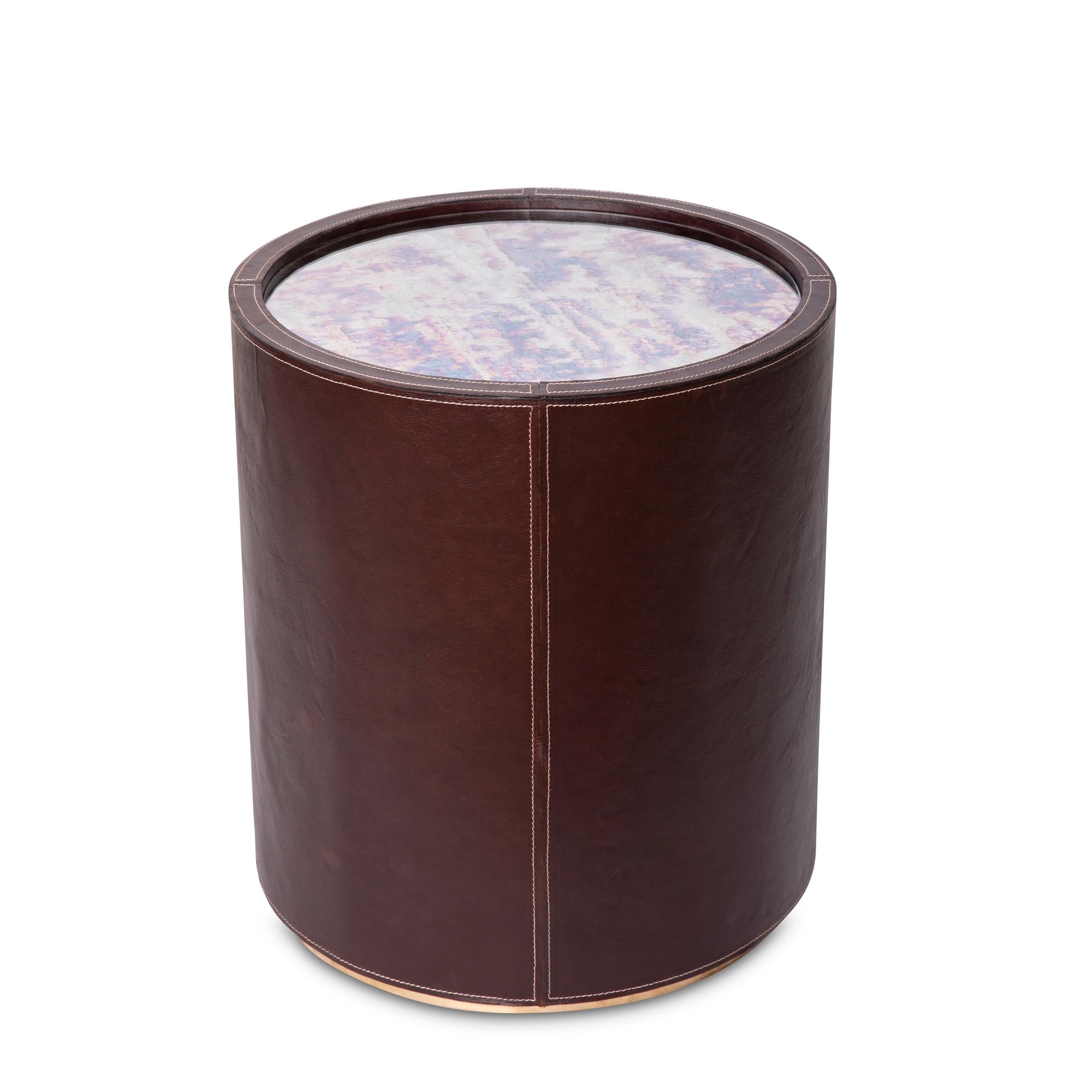 La table à boire en verre teinté Nyla est un symbole d'opulence. Elle est délicatement enveloppée de cuir véritable surpiqué. Cette pièce étonnante combine sans effort l'allure d'un miroir antique et la sophistication du cuir. L'inclusion d'une base