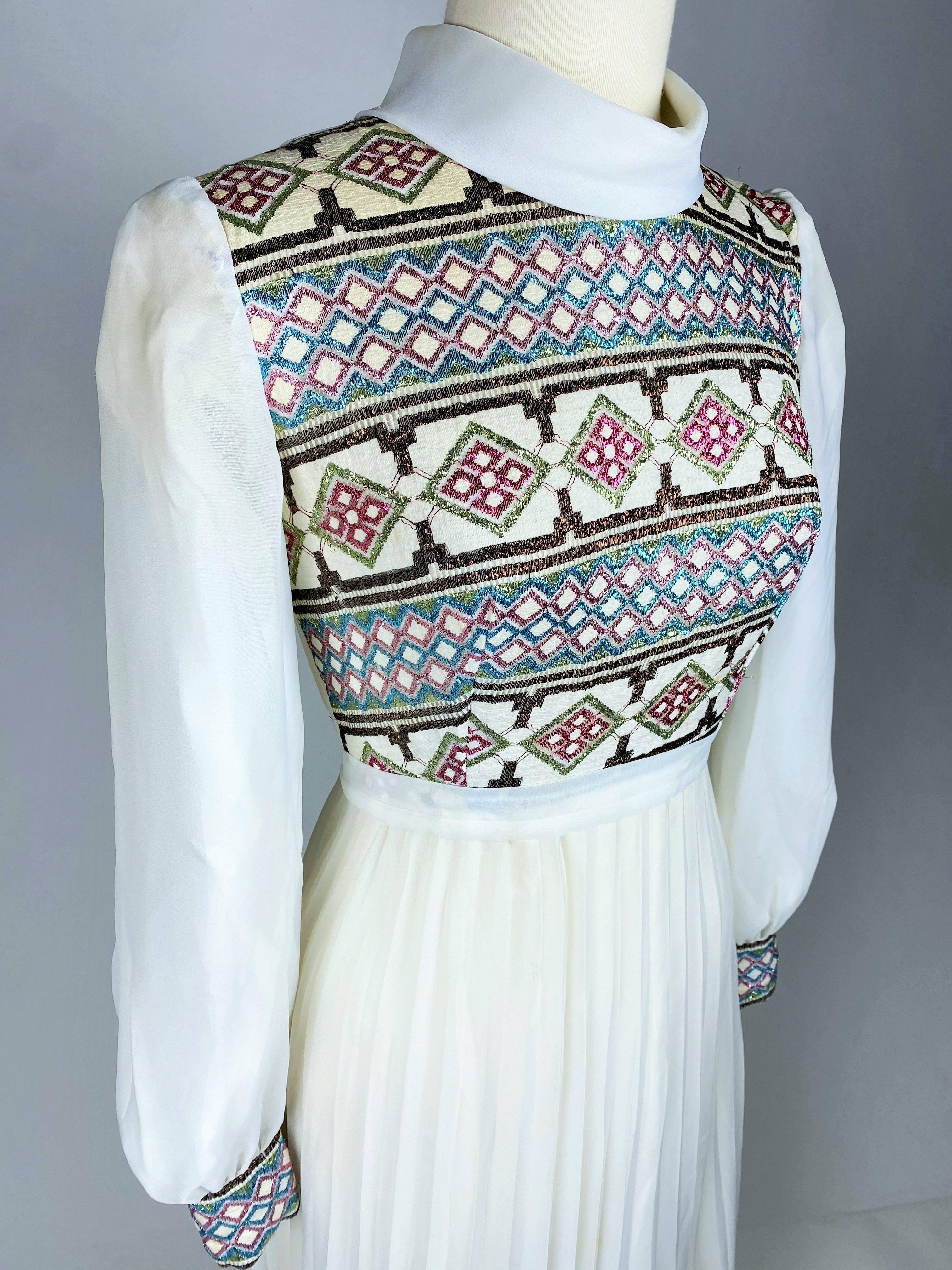 Ca. 1972

Frankreich

Langes Kleid aus cremefarbenem Nylon mit Bustier und Manschetten aus glänzendem Lurex in geometrischen Mustern für eine Feier oder eine Brautjungfer. Hoch tailliertes Kleid mit Claudine-Kragen und langen Puffärmeln. Breiter
