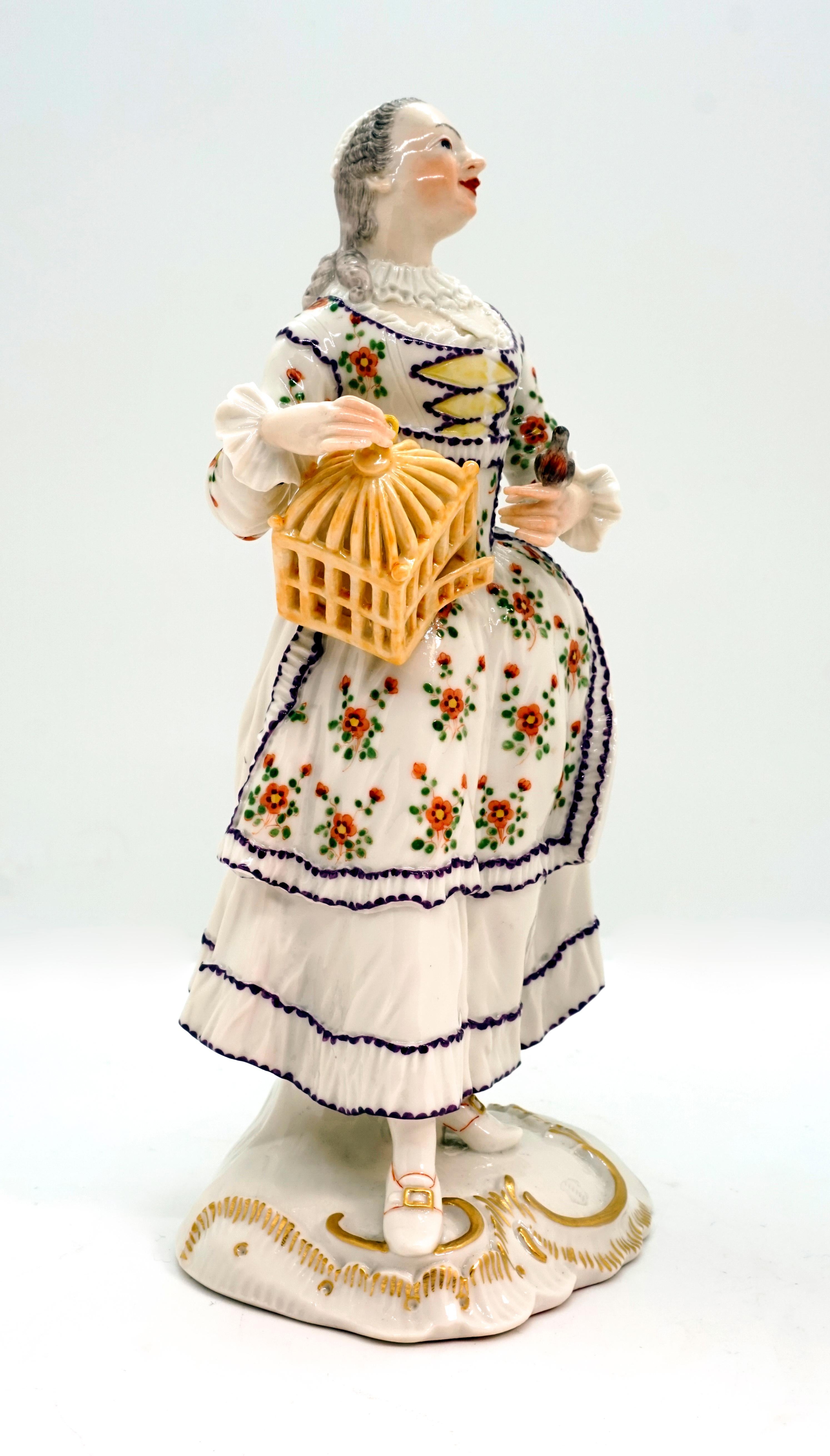Figurine très rare de l'ancien fabricant Frankenthal Allemagne.
La dame, habillée dans le style rococo : robe blanche avec corsage et tablier fleuris, bonnet blanc, tient de la main droite une cage à oiseaux ouverte, posée sur sa hanche. L'oiseau