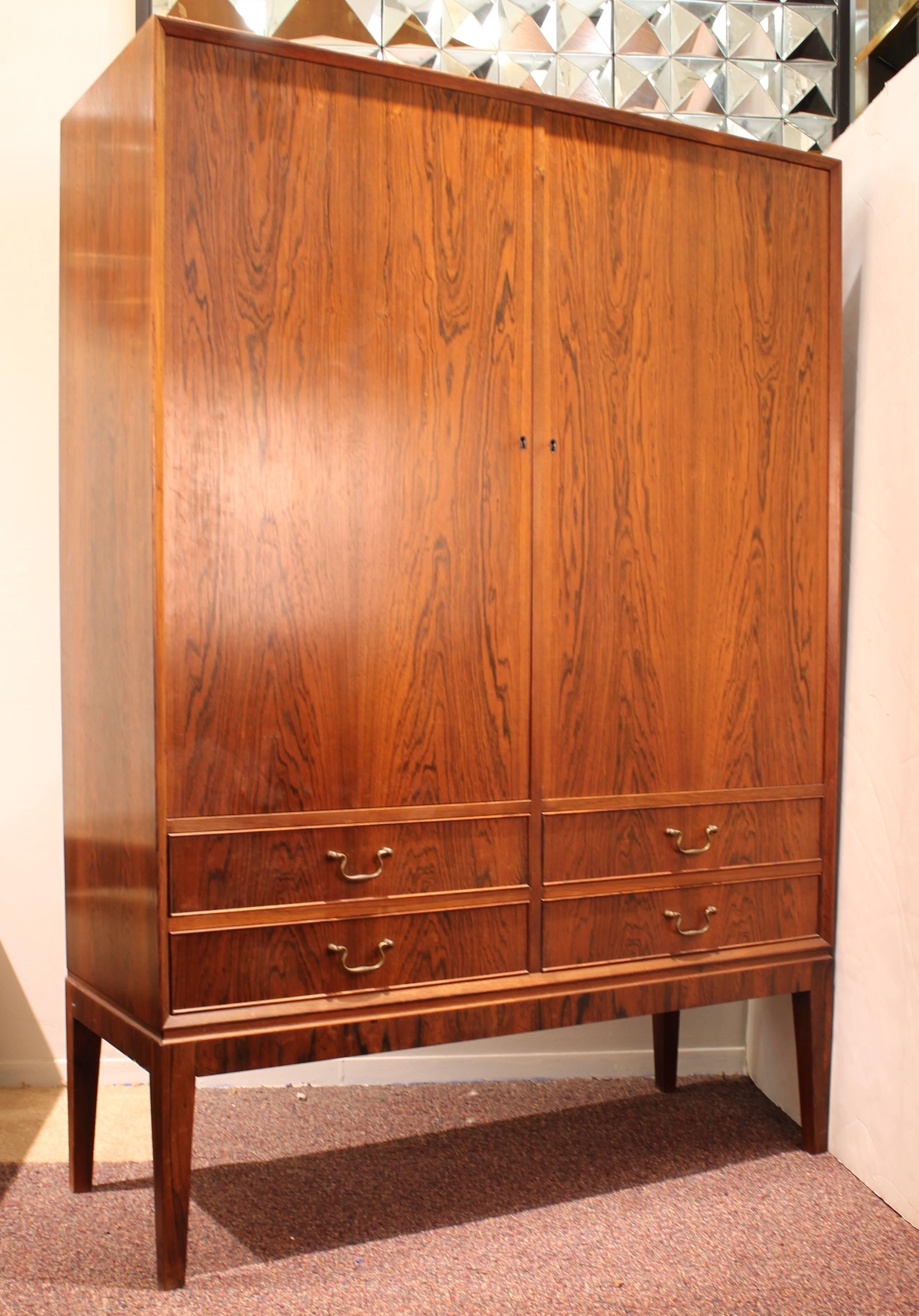 A Mid-Century Modern storage cabinet made in circa 1955 in Denmark by the O. Bank Larsen Mobelfabrik. The piece is made in solid rosewood with custom brass hardware and with a rosewood and red mahogany interior with adjustable shelves. In great