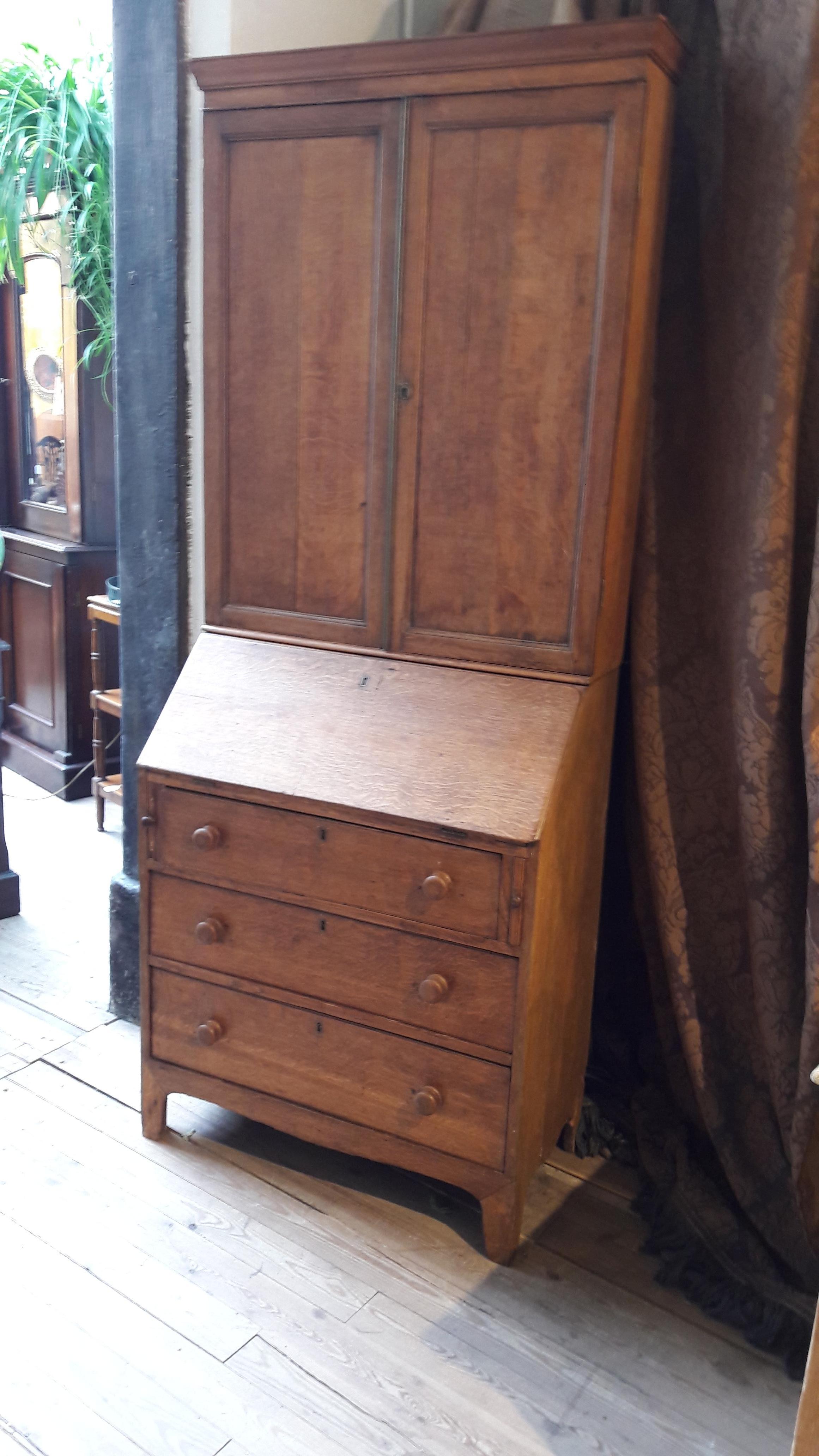Decorative and slim secretaire (bureau) bookcase in light oak. The upper part is with wooden panel doors wich is quite rare. Inside the secretaire there is a nice tan leather and some small drawers.