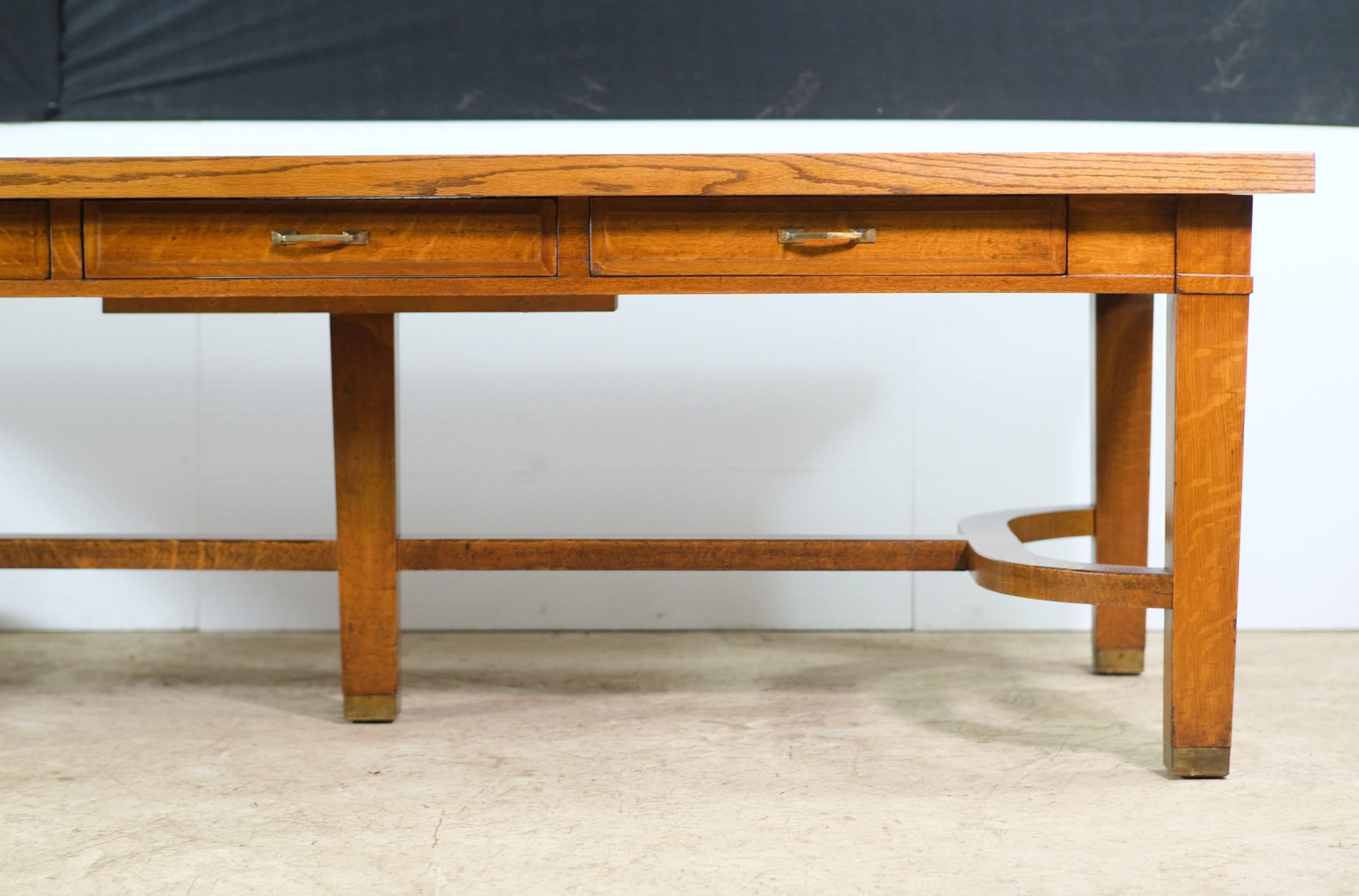 Early 20th century oak library table. Extra tall at 31 1/4 inches. Features six roomy drawers with original brass drawer pulls, three per side. Brass leg caps for protection. Also has a fifth center leg for support. Refinished with a smooth satin