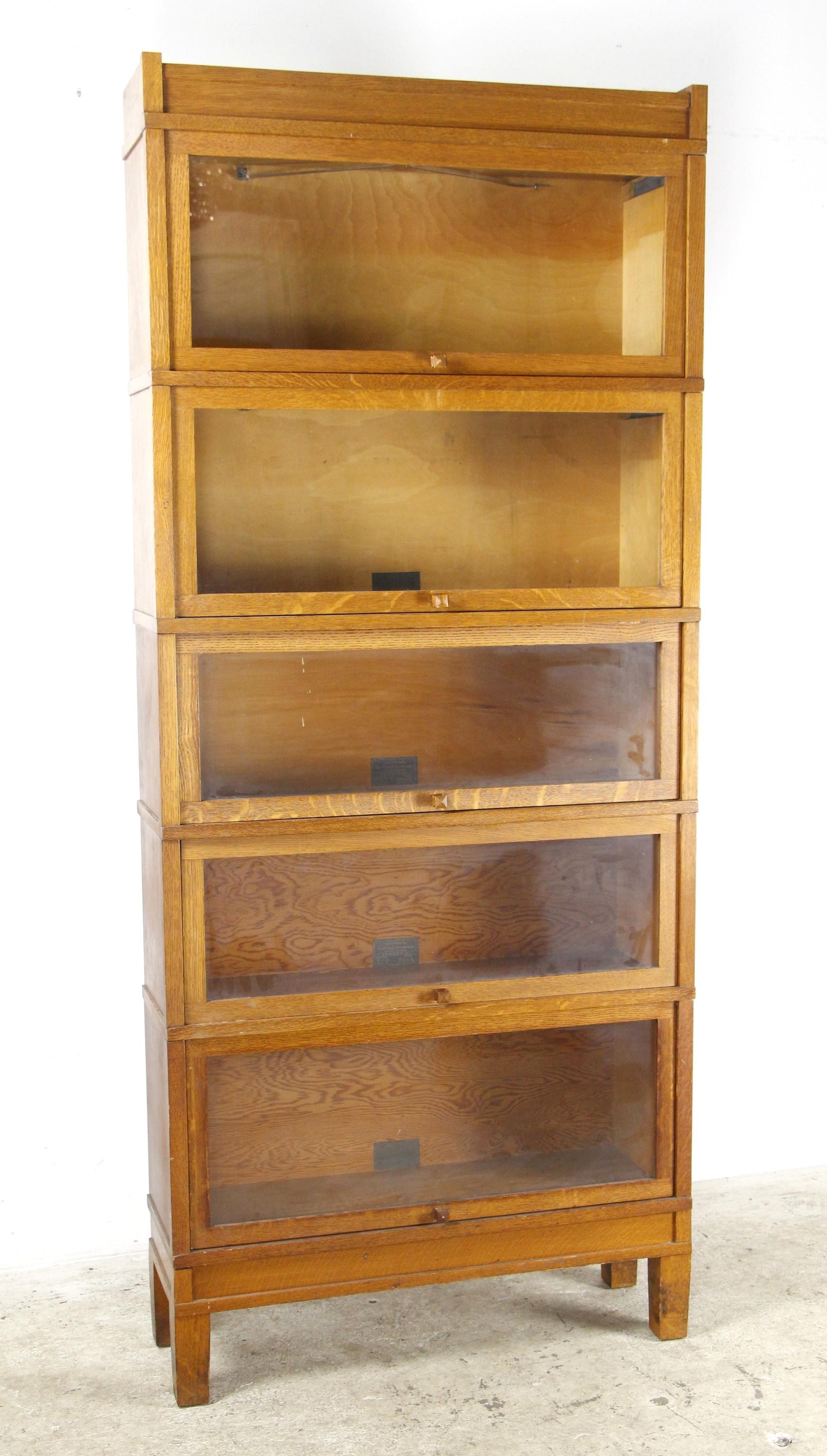 Medium tone oak bookcase with five sections and glass doors. Made 

Early 20th century five section bookcase made out of oak with a medium stain. Glass doors slide up and into each shelf unit for storage. Modular construction. Manufactured by