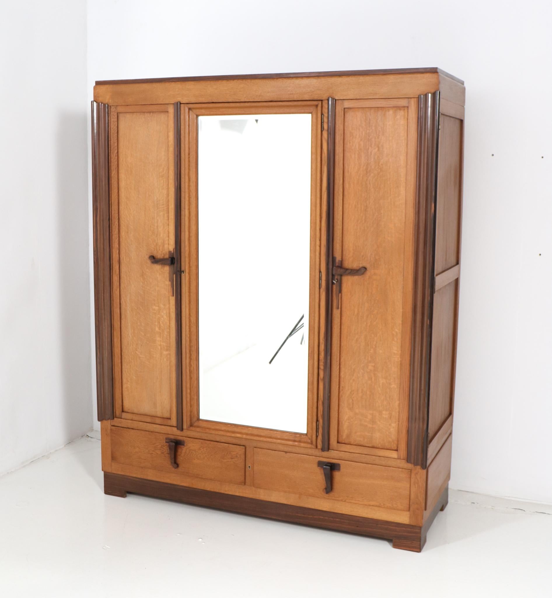 Magnificent and rare Art Deco Amsterdamse School armoire or wardrobe. Design by C.H. Eckhart Rotterdam. Striking Dutch design from the 1920s. Solid oak with original solid macassar ebony handles on doors and drawers. Original beveled glass mirror.