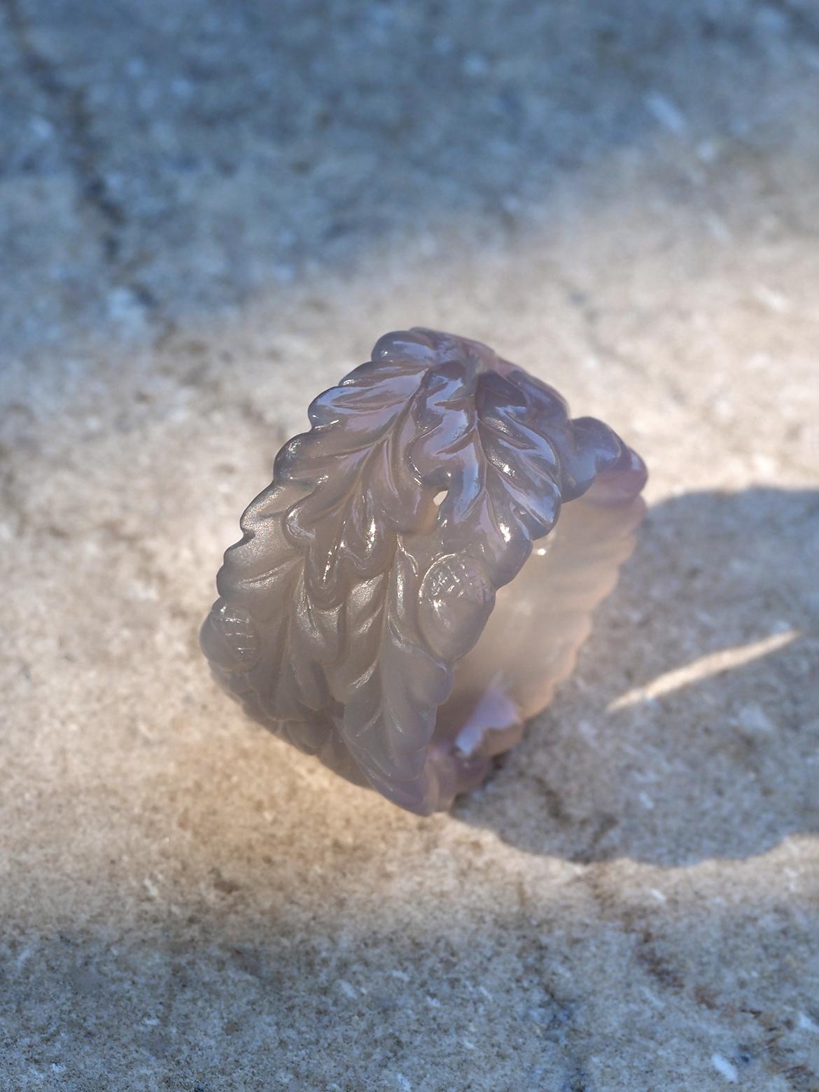 Questo eccezionale anello unico è scolpito meticolosamente in agata grigia naturale. Il suo design è caratterizzato da intricate foglie di quercia e ghiande che avvolgono la fascia, simbolo di forza e resistenza. L'anello mescola magistralmente