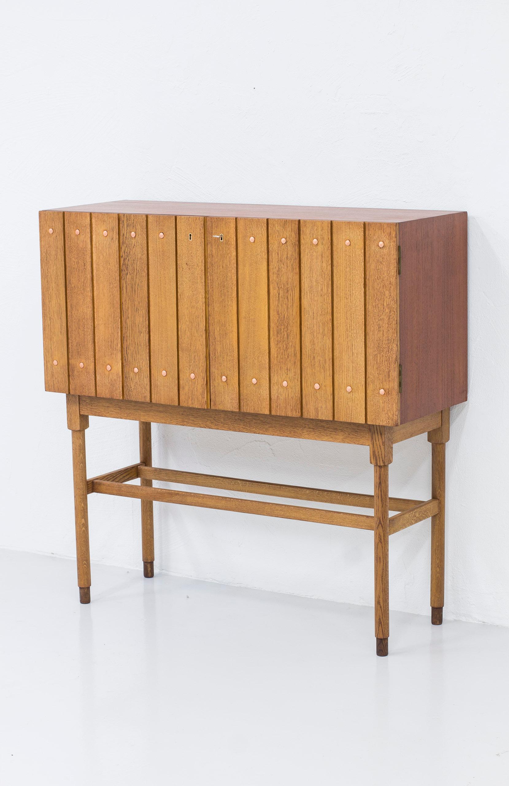 Bar cabinet designed by Bjørn Engø. Produced in Norway by Gustav Bahus during the 1940-50s. Made from teak and doors of solid oak slats with copper nails. Base made from solid oak with contrasting oak feet. Inside of the cabinet in teak wood and
