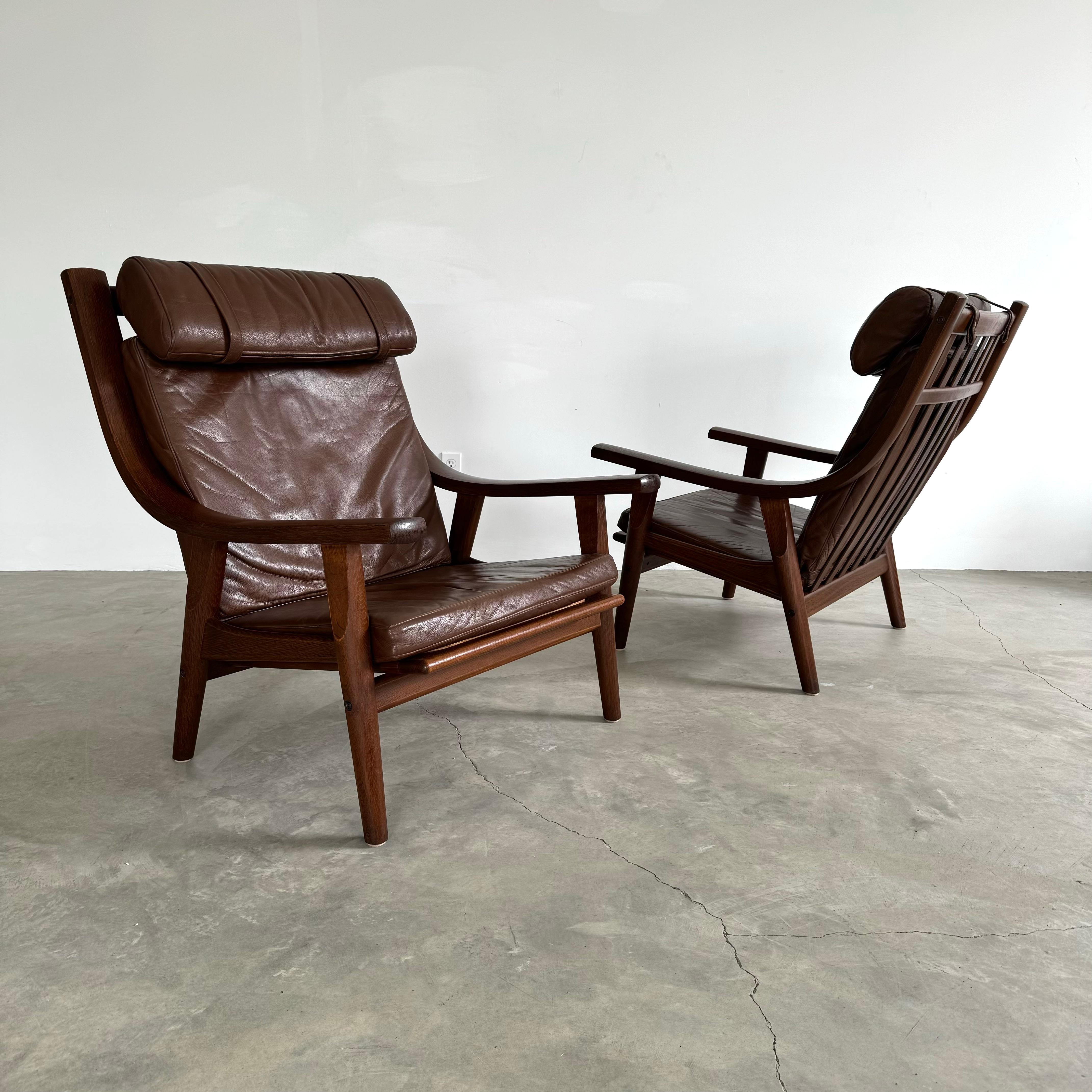 Excellent pair of oak and leather armchairs designed by Hans Wegner. 1960s, Denmark. Rich, dark tone to wood recently refinished. Dark brown leather seat, backrest and neck pillow. Extremely comfortable. GE-530 chairs. Armrests were designed to