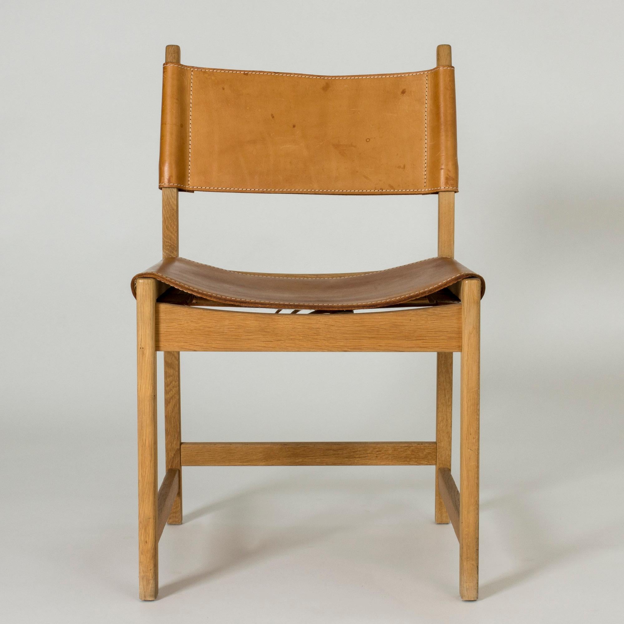 Elegant chair by Kurt Østervig, with a boxy oak silhouette and leather seat and back. Details of white seams on the sturdy, nicely patinated leather.