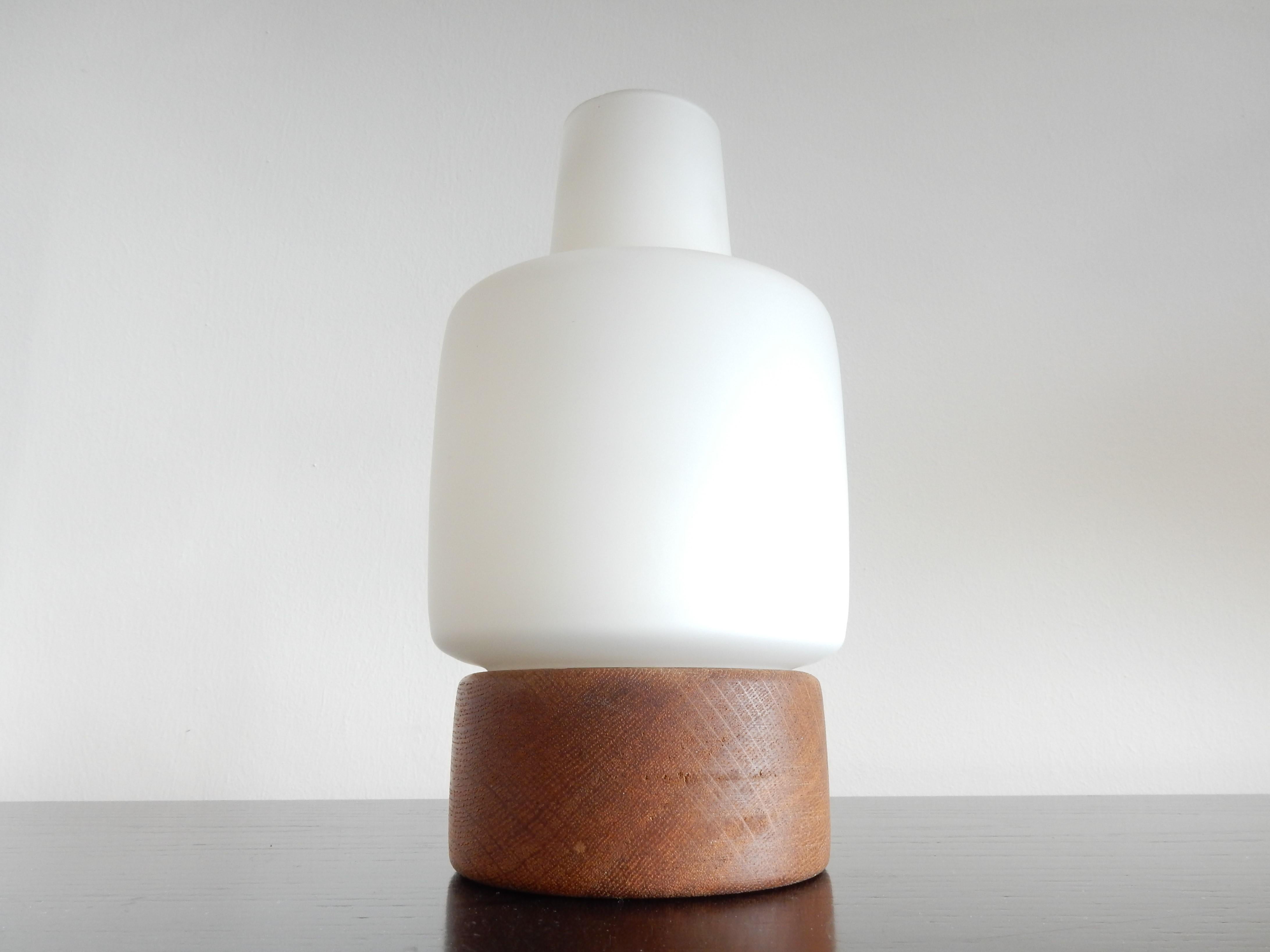 Cette jolie lampe de table, que l'on ne voit pas souvent, a été conçue par Uno et Östen Kristiansson pour Luxus en Suède, dans les années 1950. Il a une base en chêne traité à l'huile avec un abat-jour en verre opalin qui donne une belle lumière