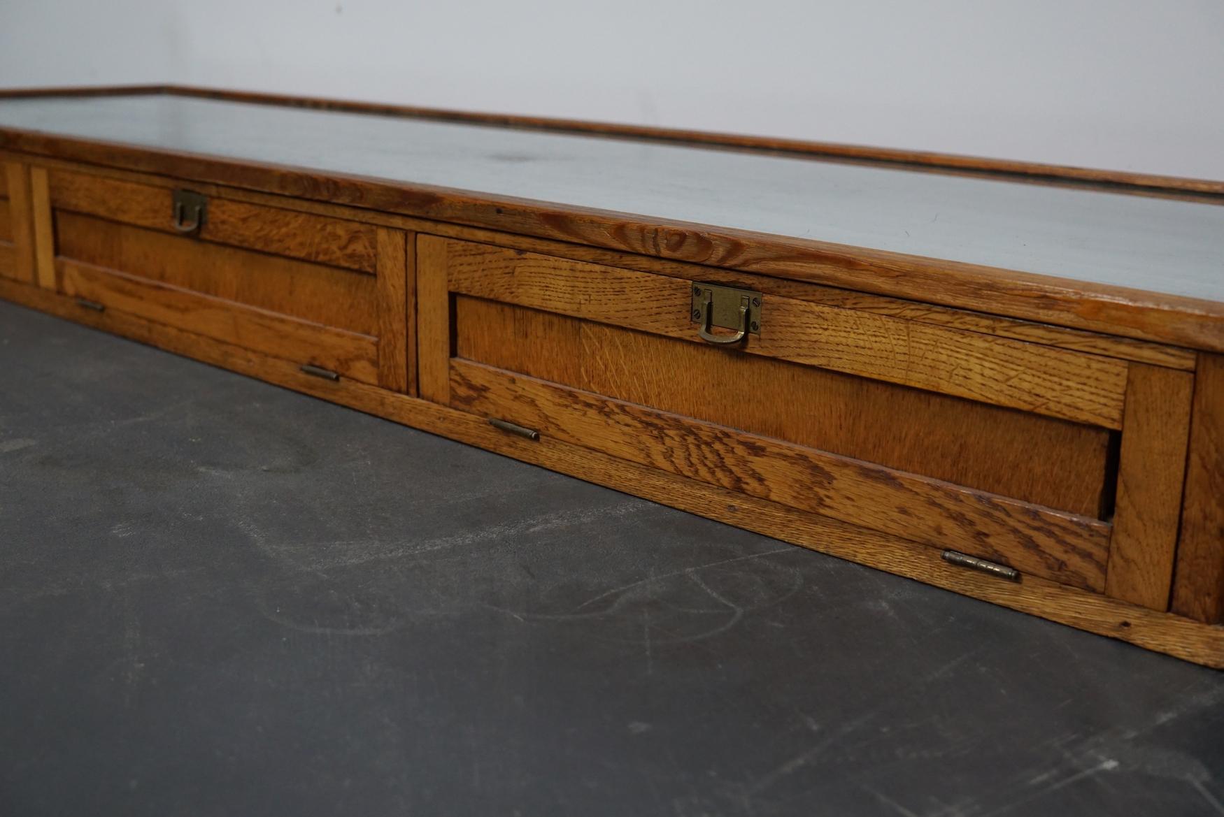 This oak counter top vitrine was made circa 1920s in England and probably used in a shop to display jewelry. It features a solid wooden frame with folding doors and brass handles. The top, sides and front are made of glass and the back of the doors