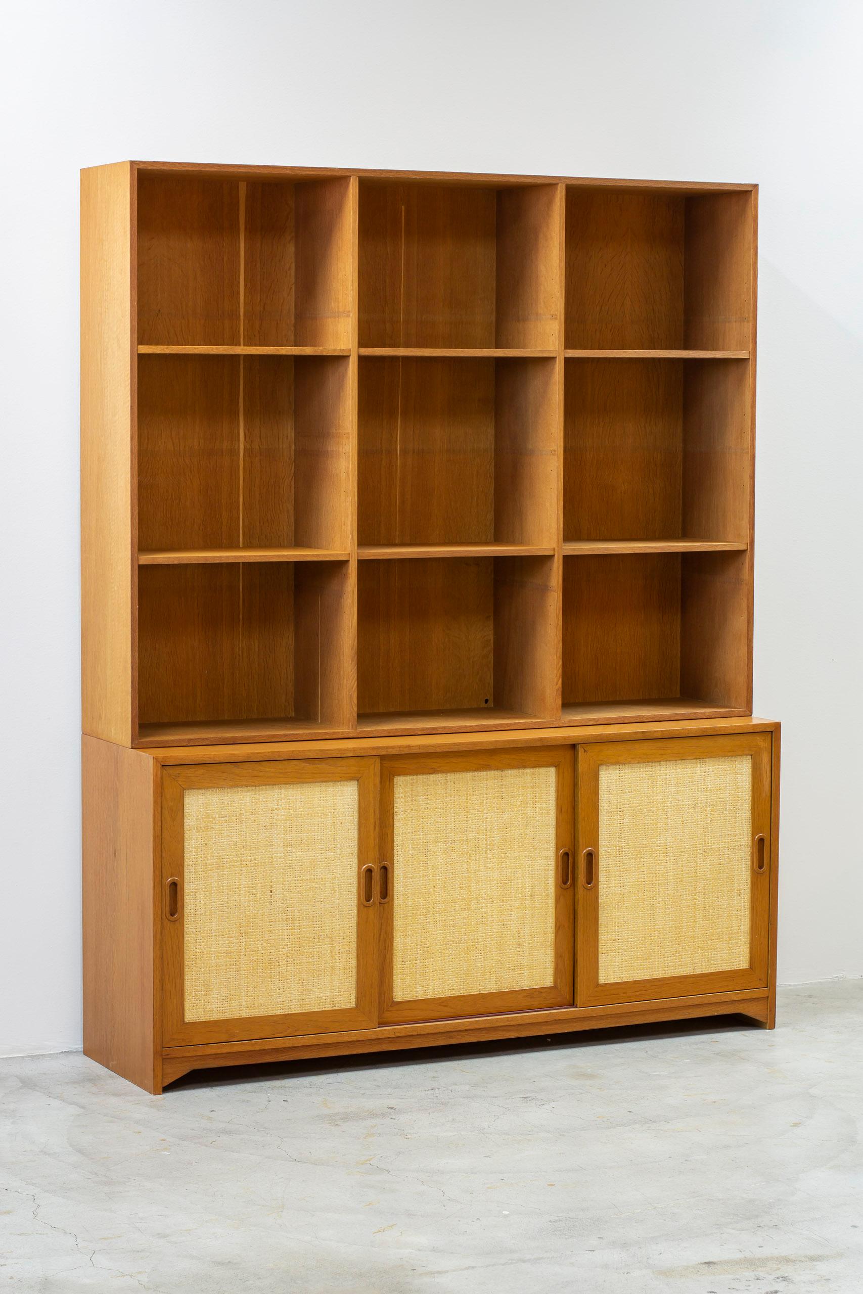 Bibliothèque conçue par Alf Svensson. Produit dans les années 1950 en Suède par Bjästa Snickeri. La partie buffet est en teck et les portes coulissantes sont en rotin. L'intérieur du buffet est en bouleau clair contrastant. L'étagère est en chêne.