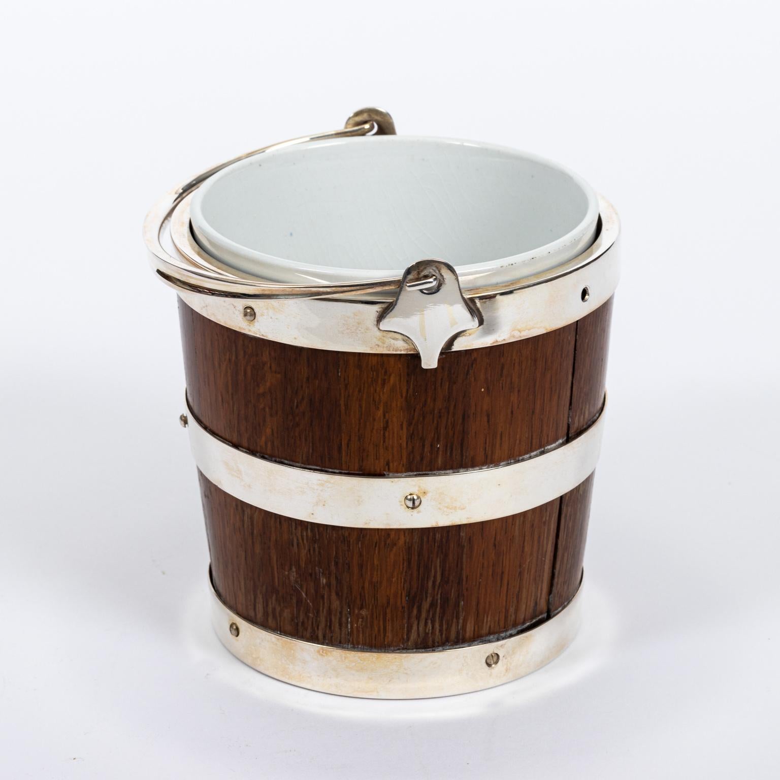 Oak and silver plate ice pail with liner, circa 1930s. The bottom of the inside of the pail features a removal silver plate flower motif panel. Please note of wear consistent with age including minor finish loss to the wood and liner.