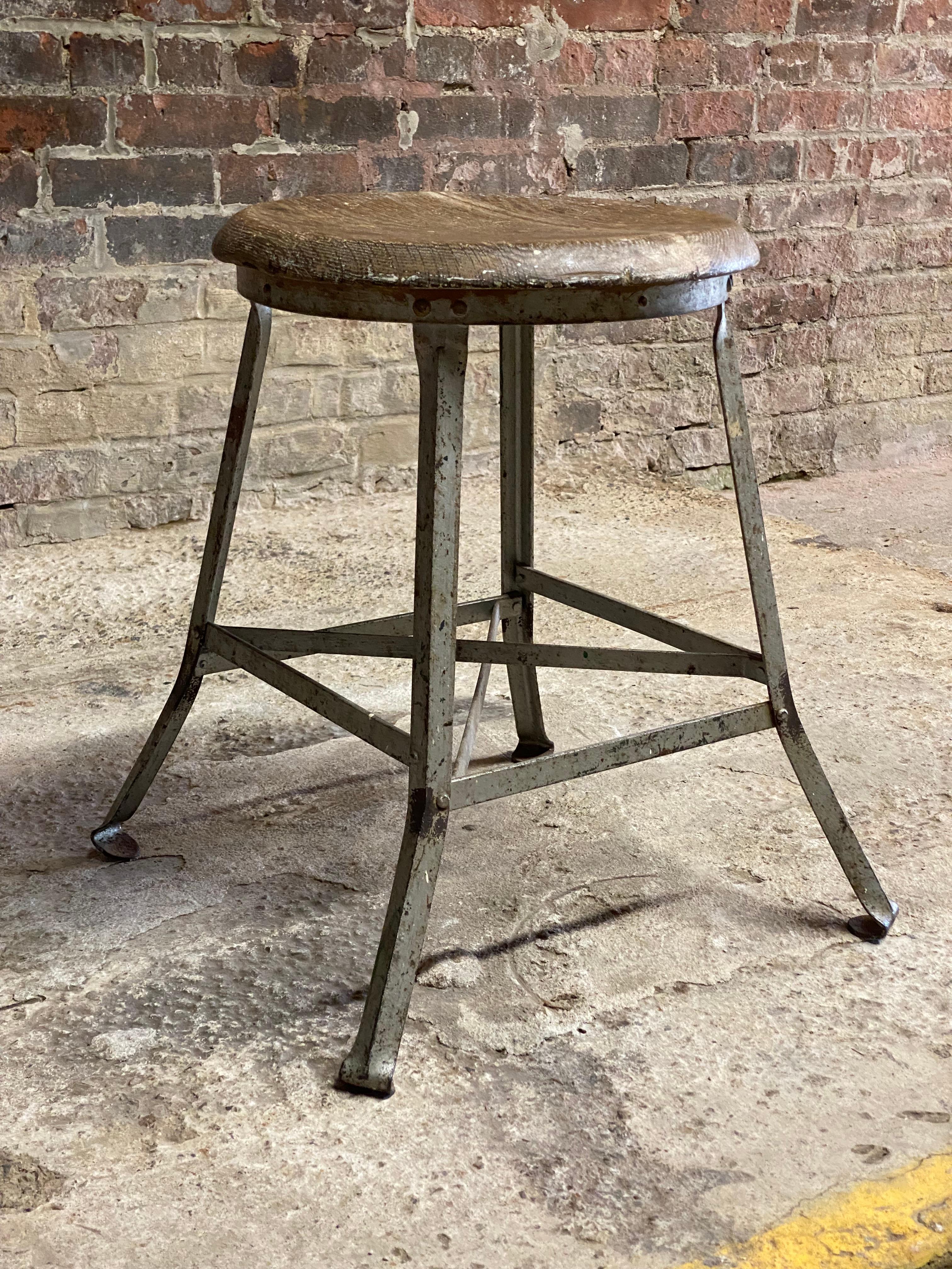 Period industrial low stool. Round oak seat with a steel base splayed legs with turned in feet. X base stretcher for maximum durability and strength. Circa 1910-1930. Good overall condition with cosmetic wear. Weathered with minor rust, finish