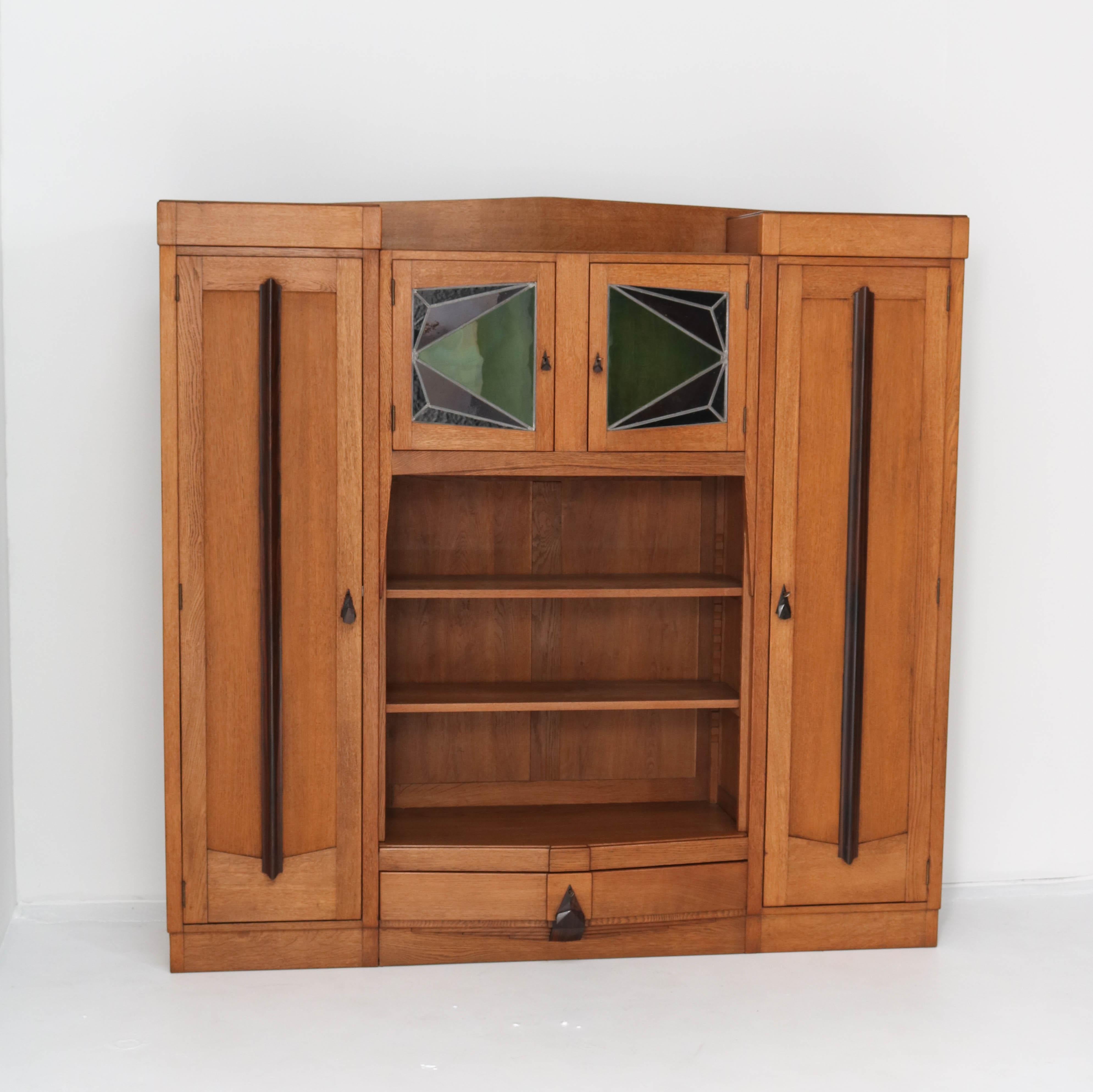 Magnificent and rare Art Deco Amsterdam School bookcase.
Striking Dutch design from the 1920s.
Solid oak with original Macassar ebony handles and lining.
The two small doors still have the original stained glass.
Ten original solid oak shelves